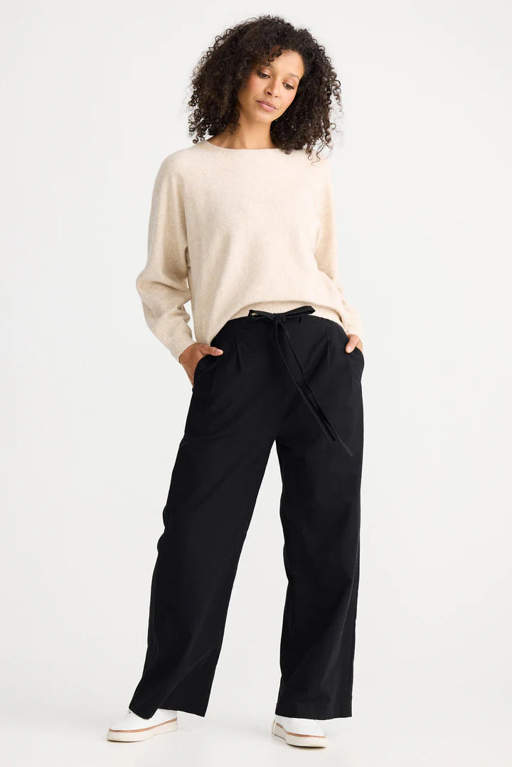 Image of Woman wearing a beige sweater and The Shanty Corporation black pants on a white background
