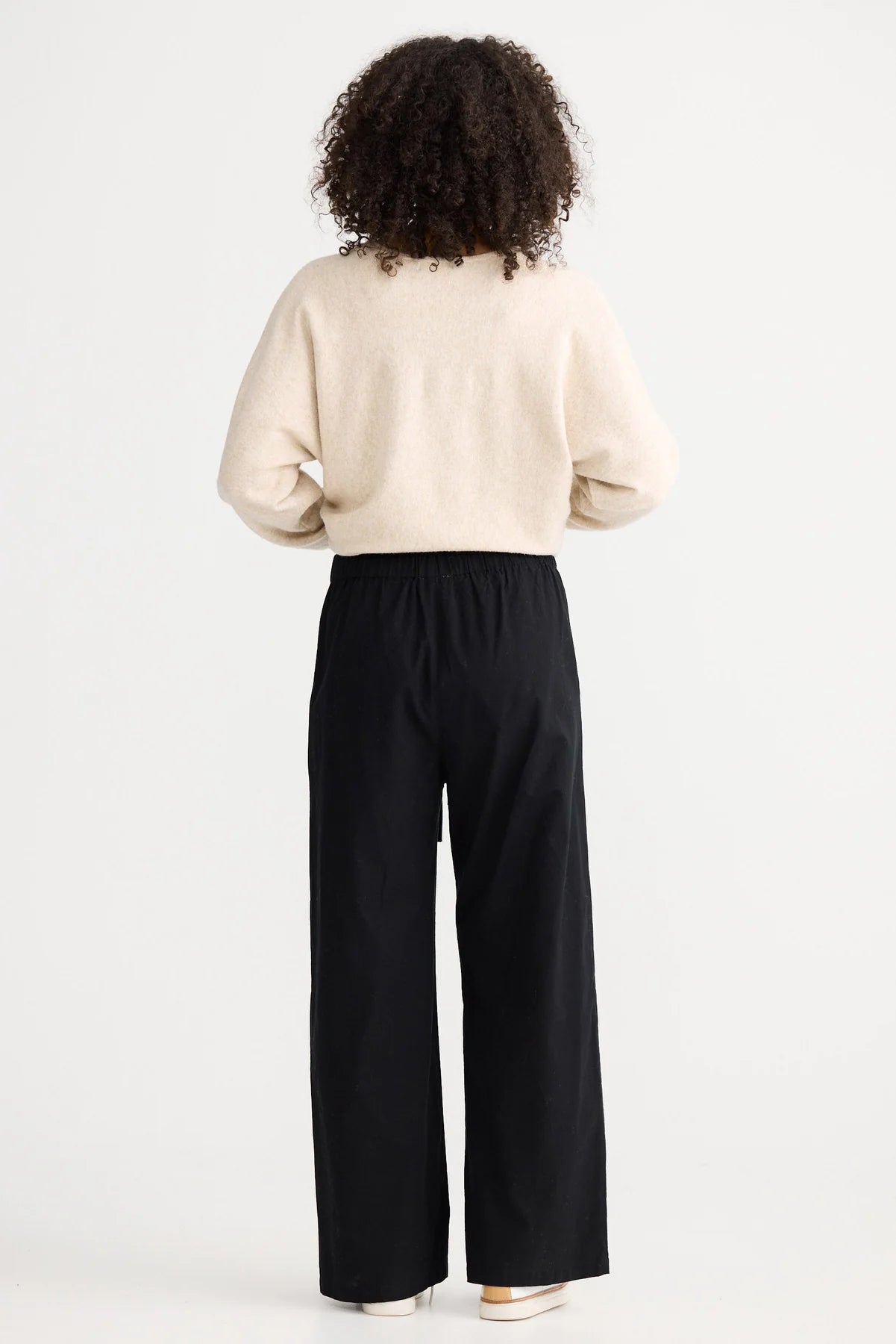Image of Woman wearing a beige sweater and The Shanty Corporation black pants on a white background