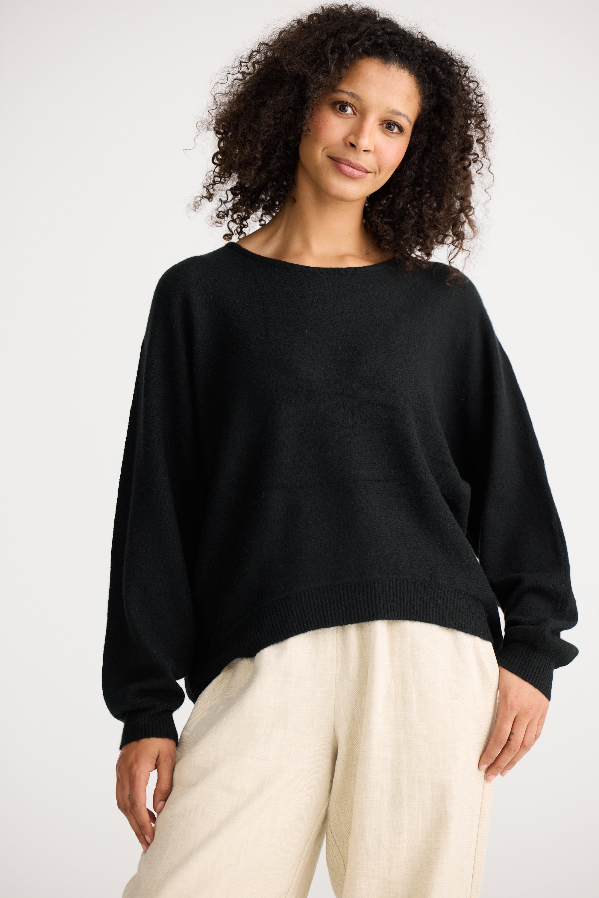 Image of Woman wearing a Shanty Corporation black sweater and beige pants on a white background