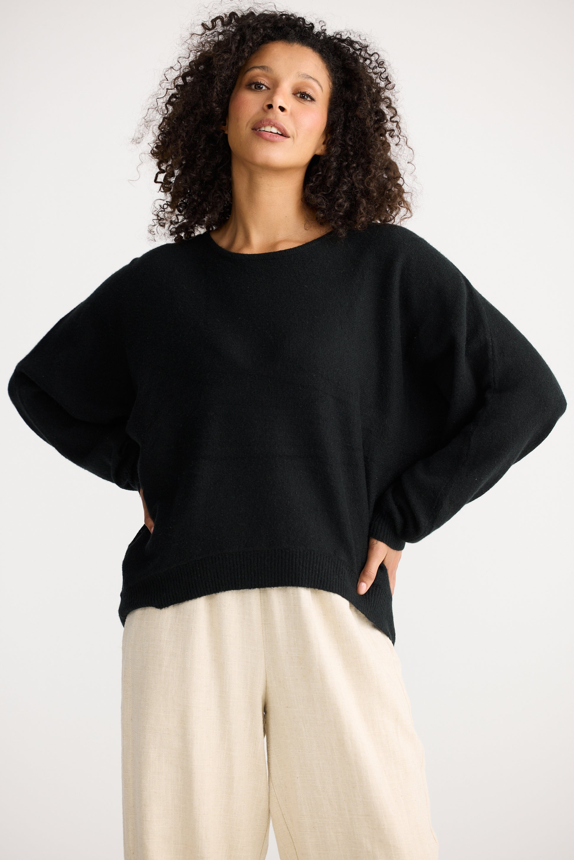 Woman wearing a Shanty Corporation black sweater and beige pants against a white background