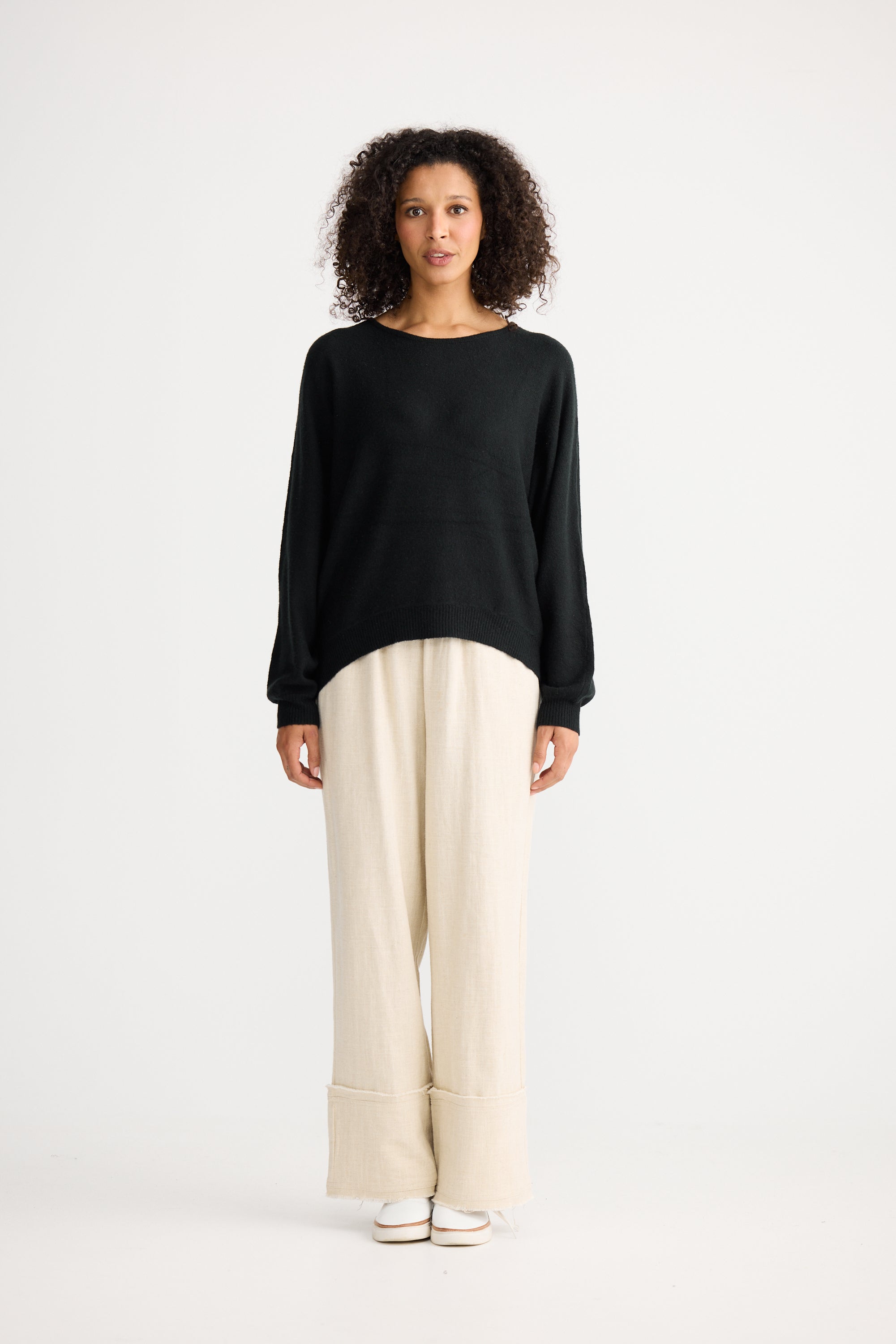 Image of Woman wearing a Shanty Corporation black sweater and beige pants on a white background