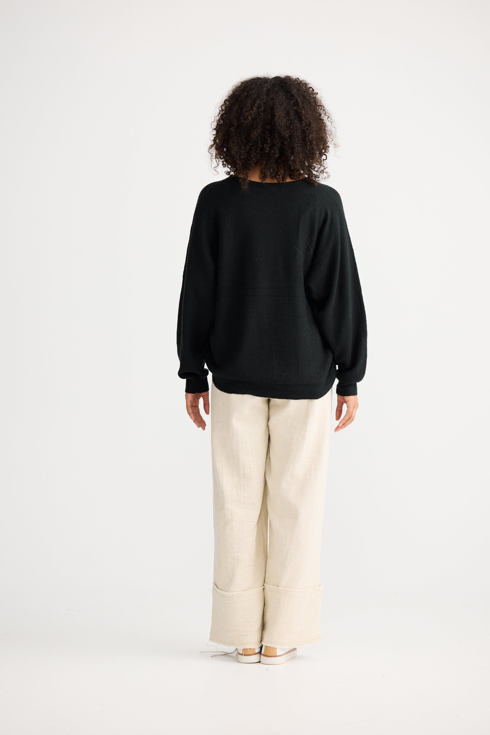 Woman wearing a Shanty Corporation black sweater and beige pants on a white background