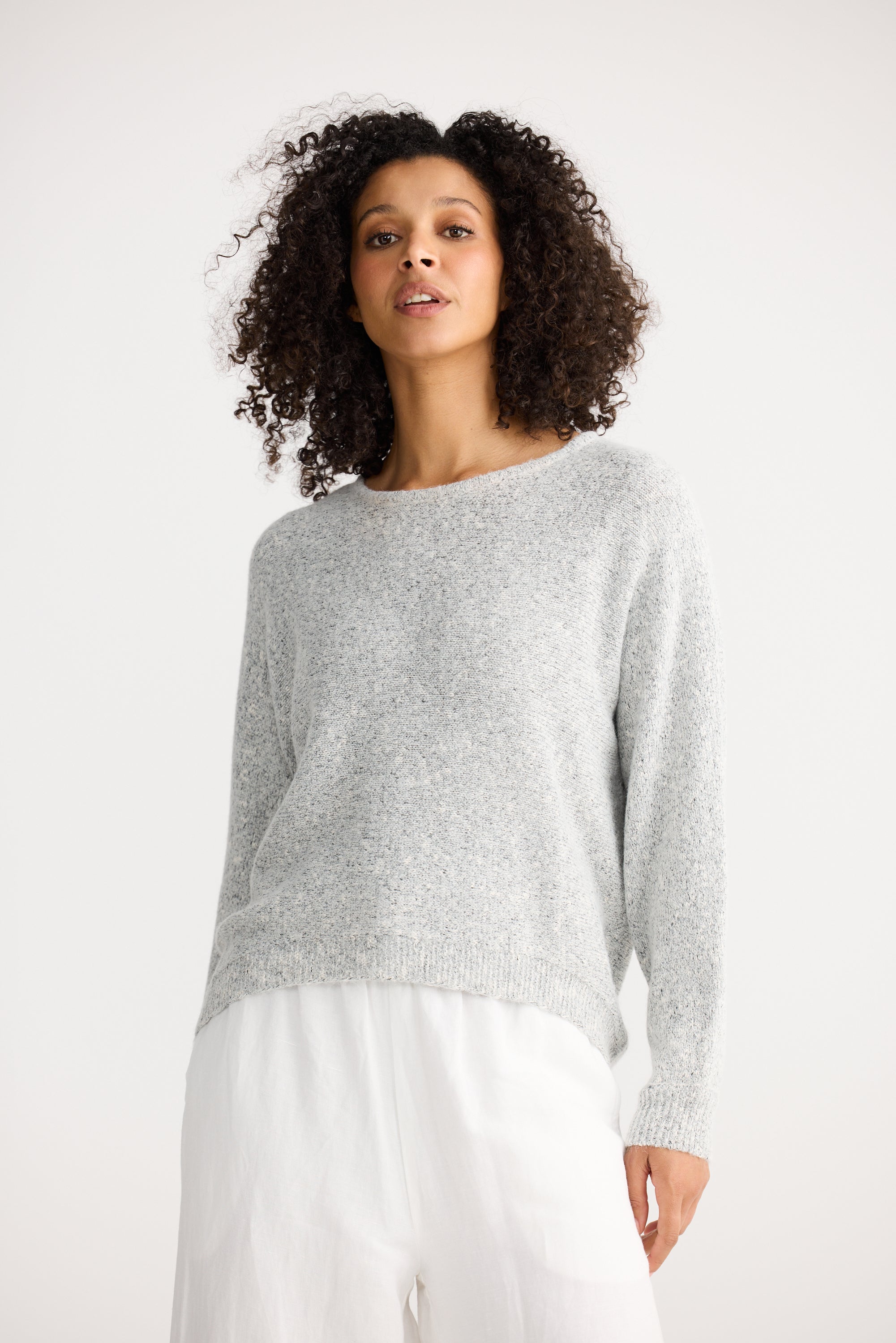 Image of Woman wearing a Shanty Corporation grey sweater and white pants on a white background