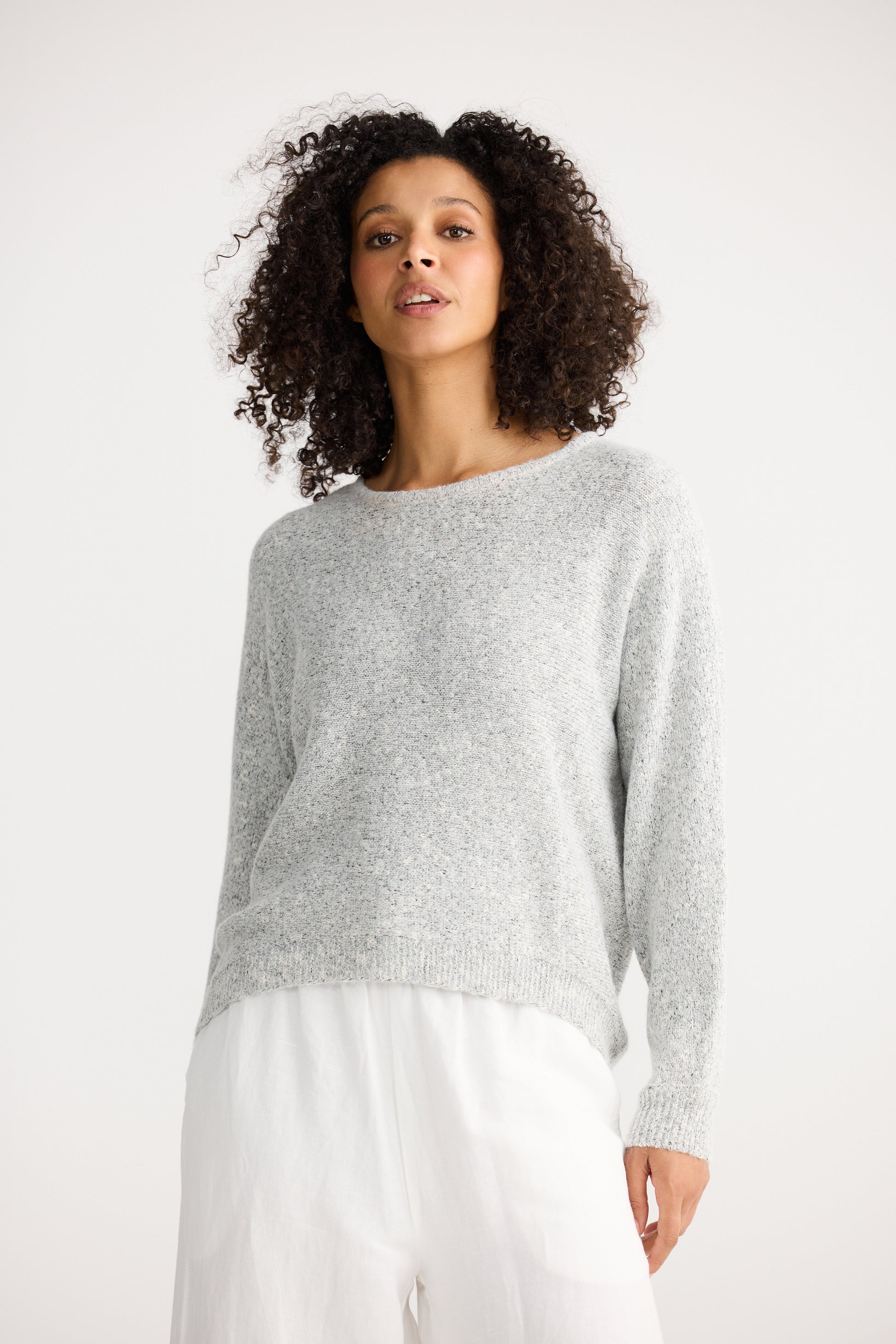 Woman wearing a Shanty Corporation grey sweater and white pants on a white background