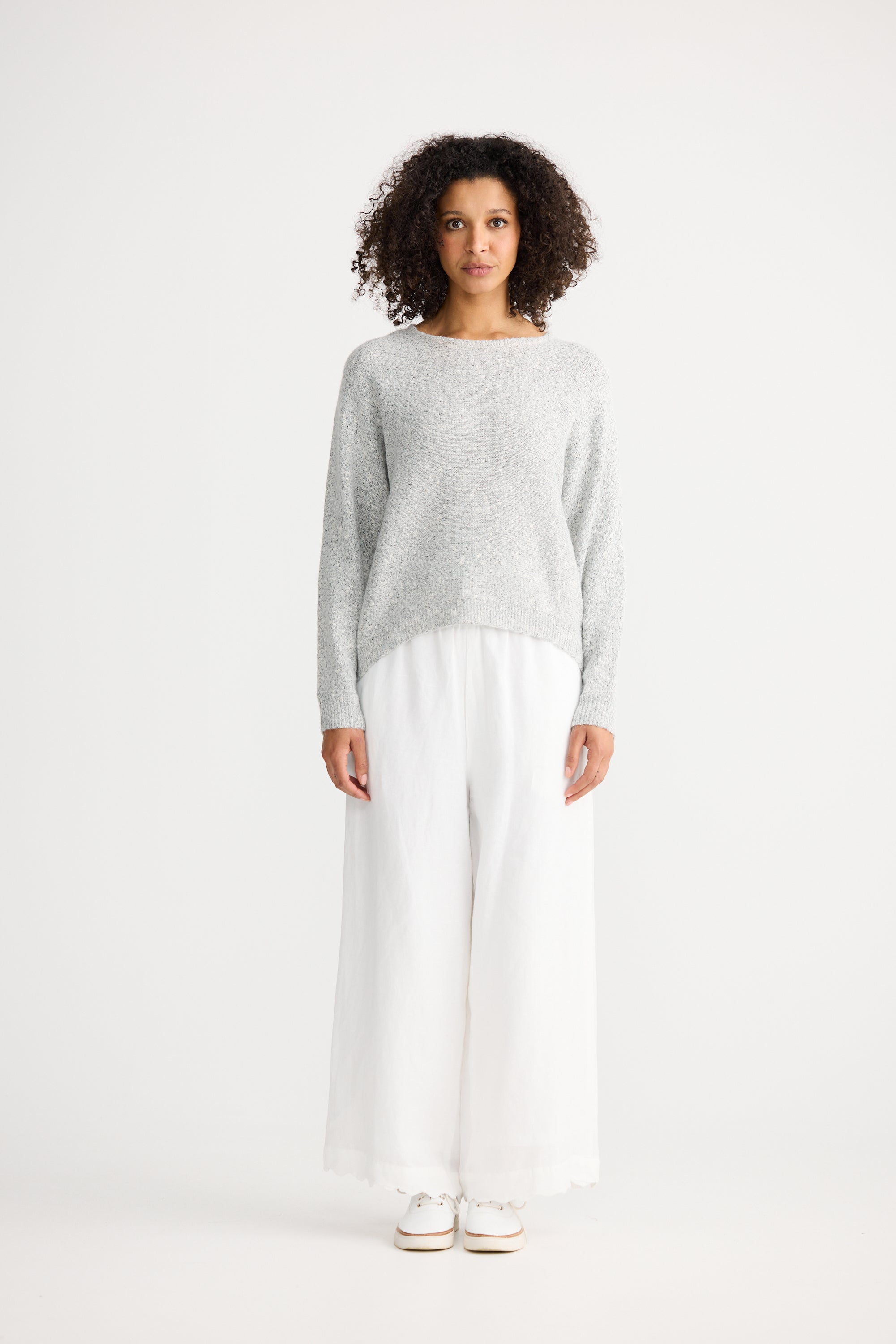 Image of Woman wearing a Shanty Corporation grey sweater and white pants on a white background
