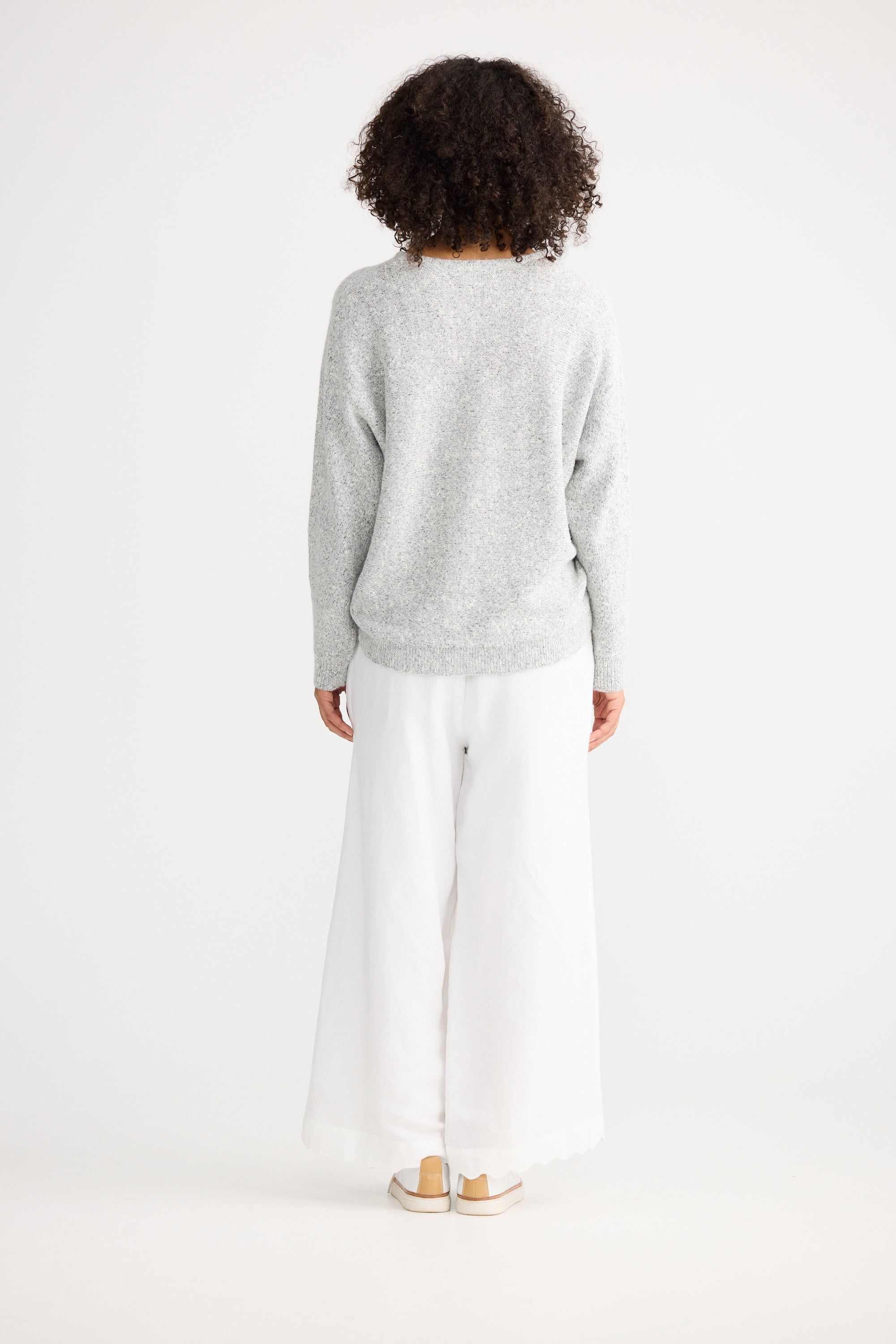 Image of Woman wearing a Shanty Corporation grey sweater and white pants on a white background
