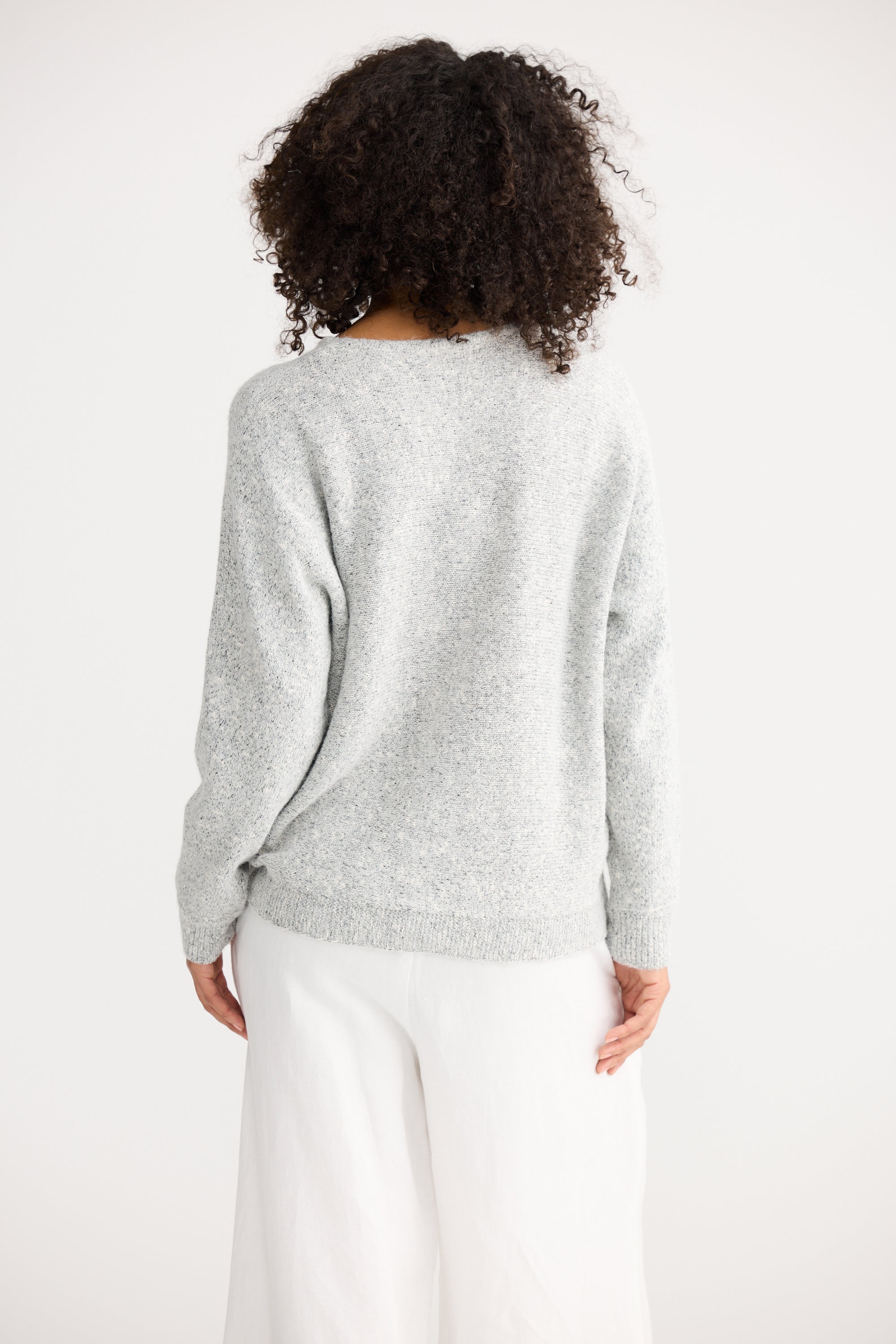 Image of Woman wearing a Shanty Corporation light grey sweater and white pants on a plain background