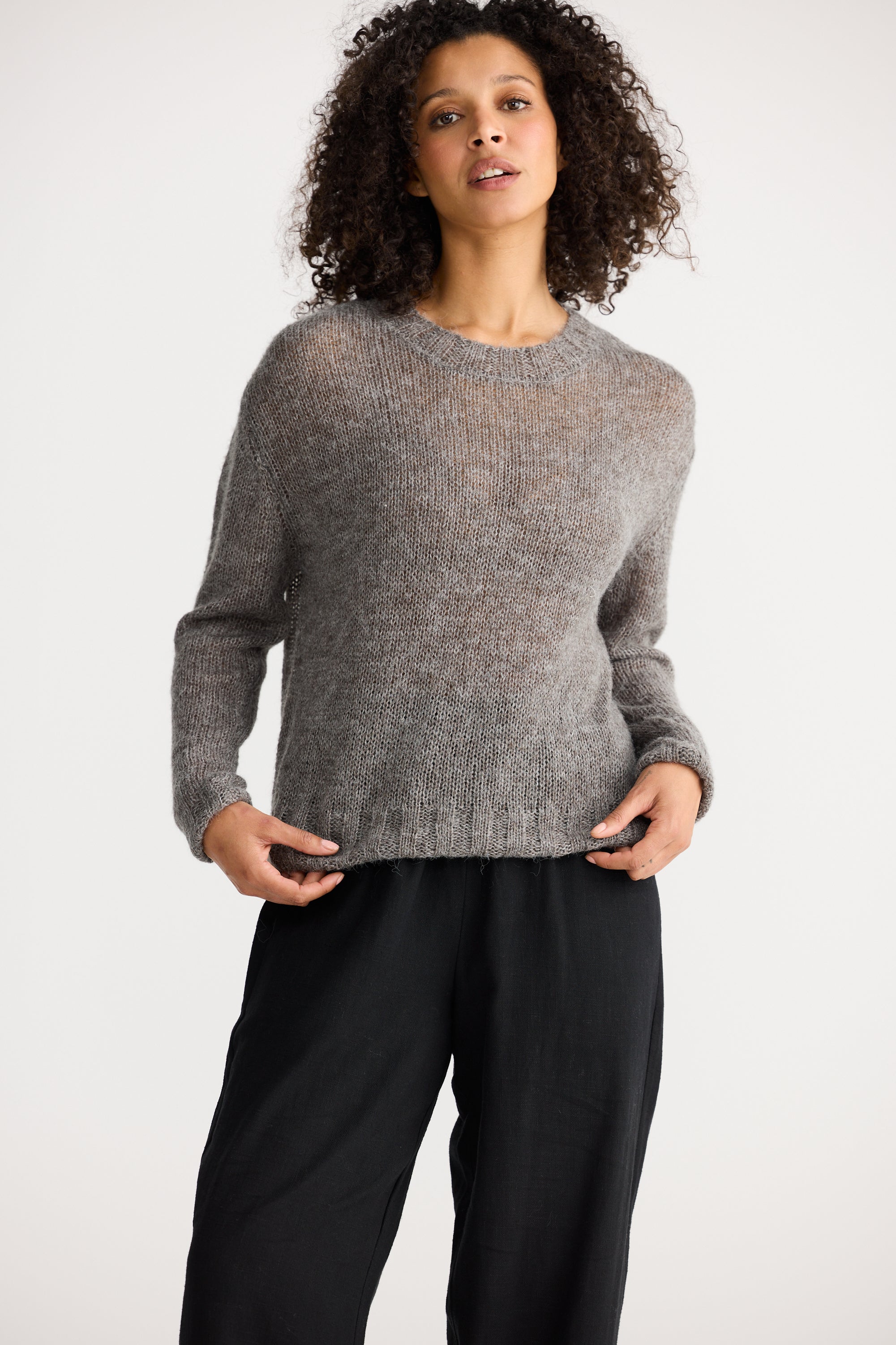 Image of Woman wearing a Shanty Corporation grey sweater and black pants on a white background