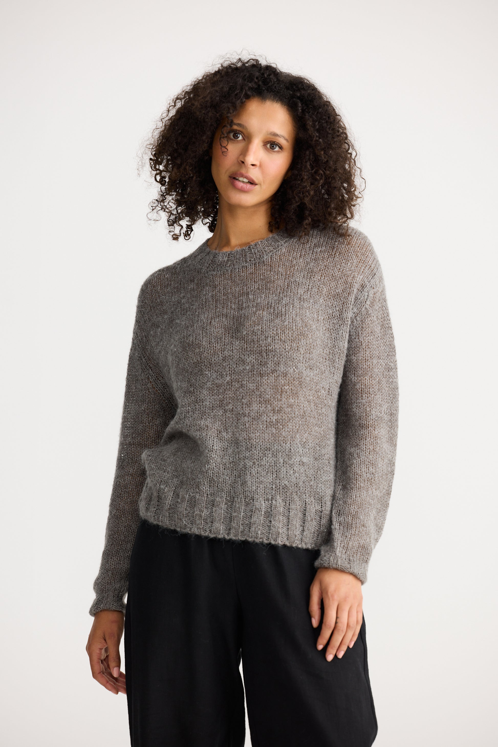 Woman wearing a Shanty Corporation grey sweater and black pants on a white background