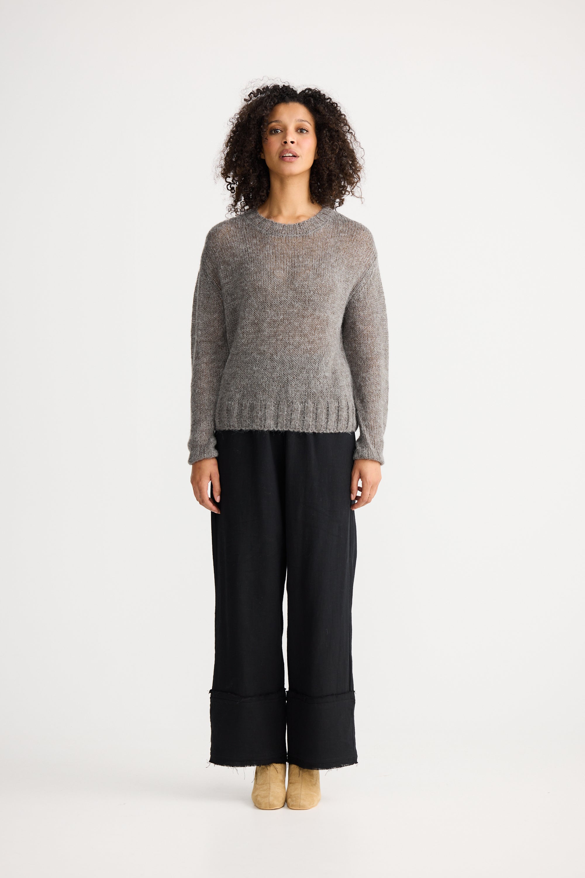 Image of Woman wearing a Shanty Corporation grey sweater and black pants on a white background