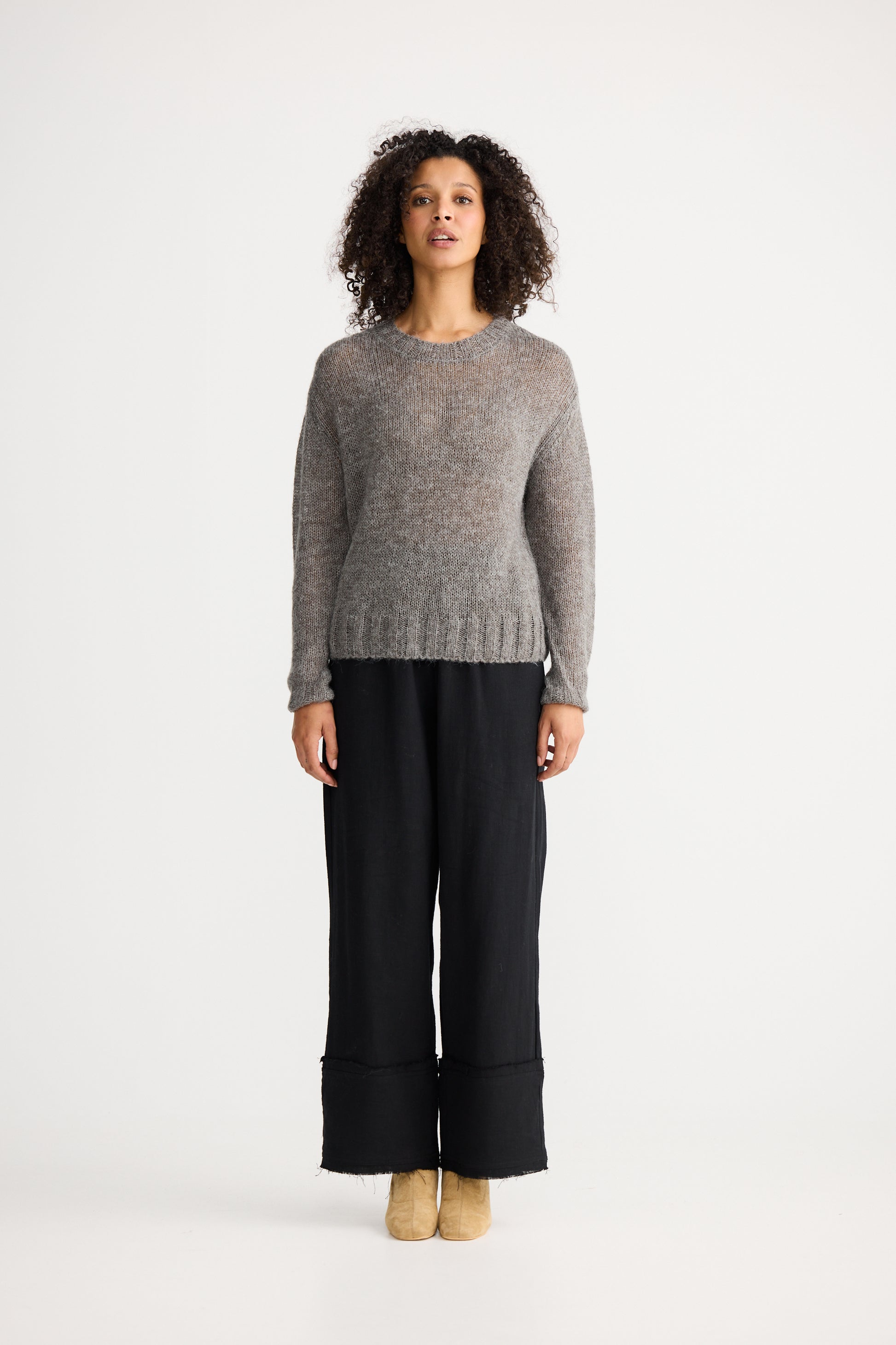 Woman wearing a Shanty Corporation grey sweater and black pants on a white background