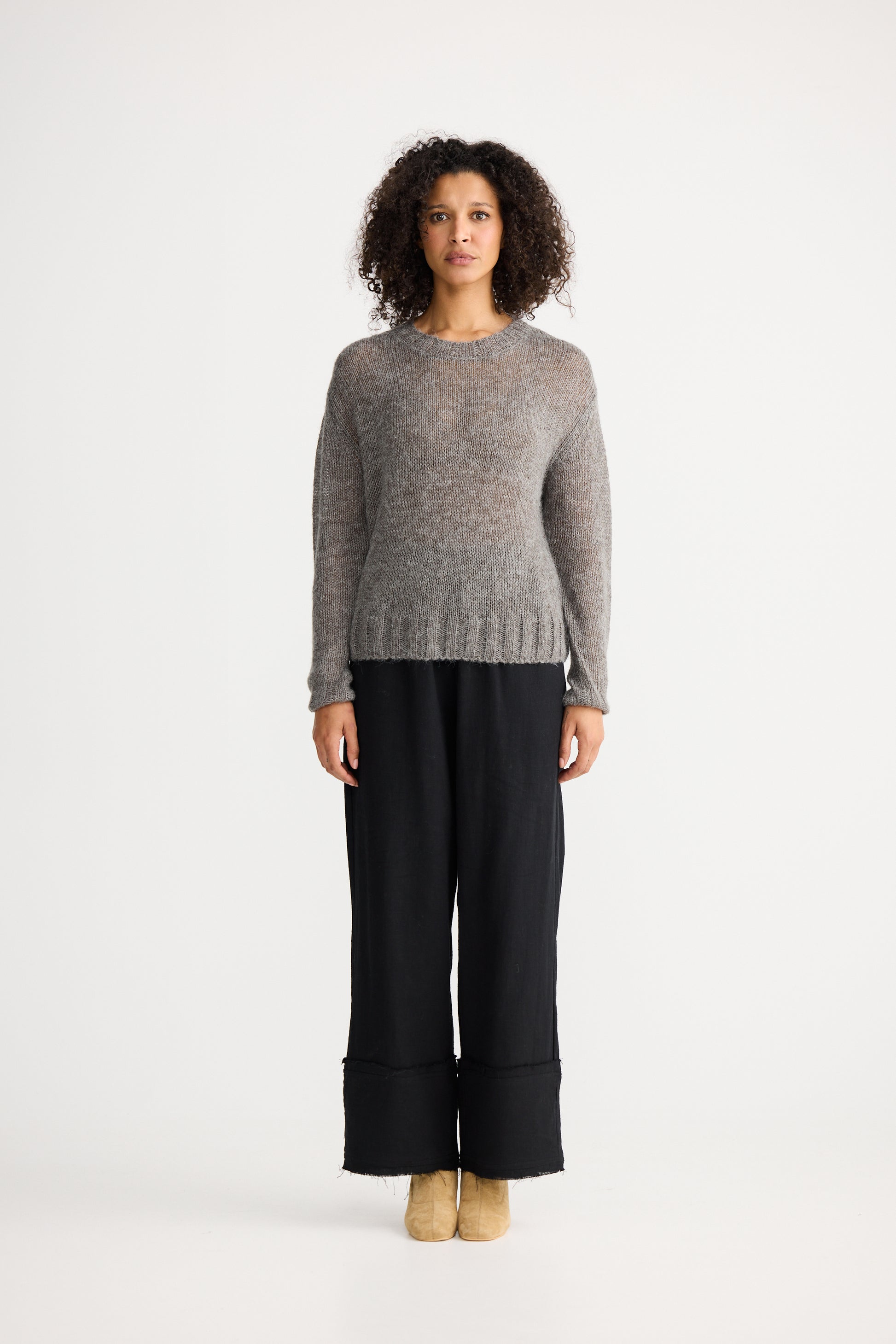 Woman wearing a Shanty Corporation grey sweater and black pants on a white background