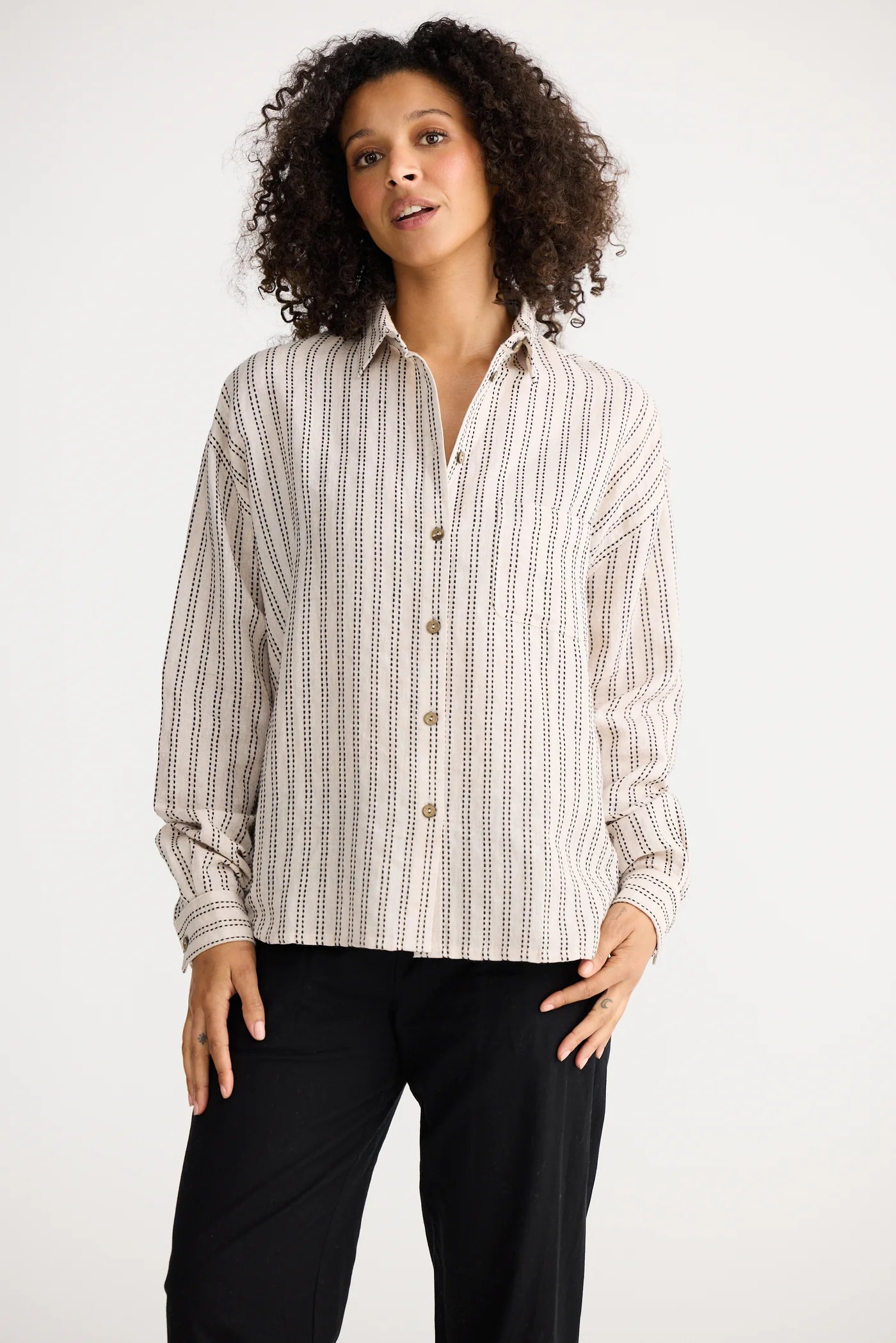 Woman wearing a The Shanty Corporation striped shirt and black pants on a white background