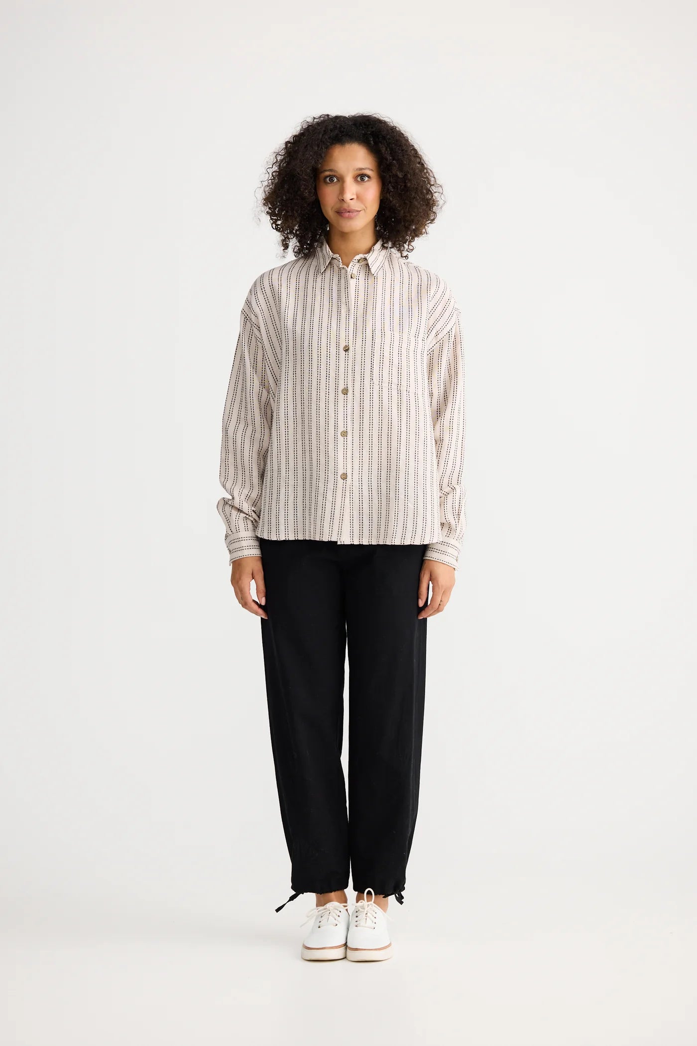 Image of Woman wearing a The Shanty Corporation striped shirt and black pants on a white background
