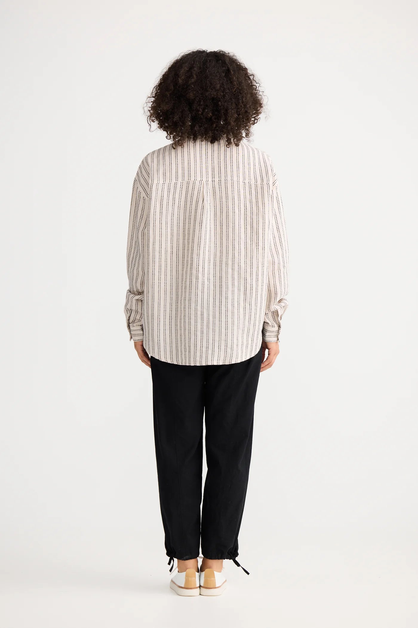 Woman wearing a The Shanty Corporation striped shirt and black pants on a white background