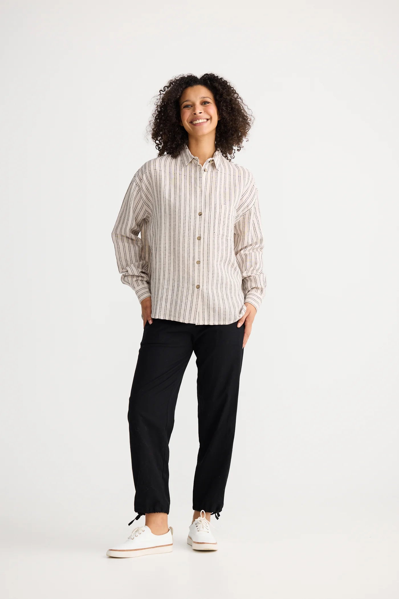 Woman wearing a The Shanty Corporation striped shirt and black pants on a white background