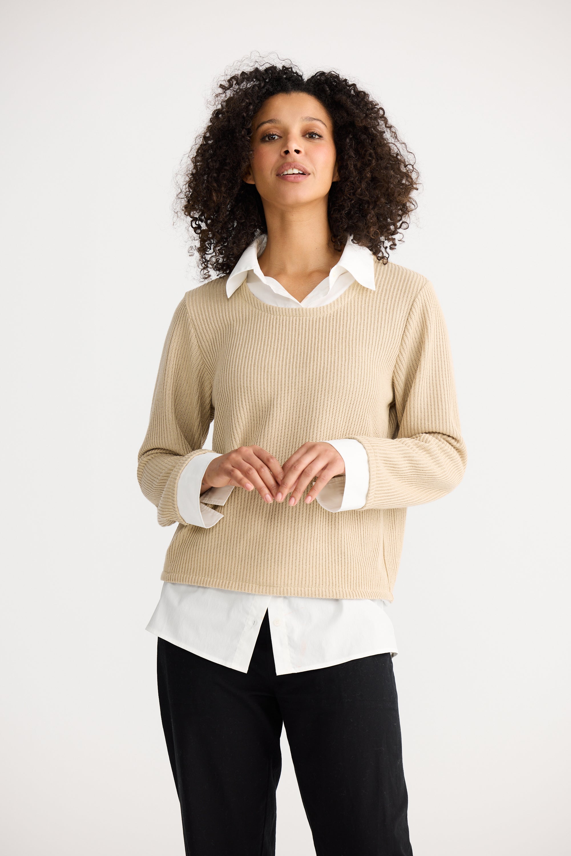 Image of Woman wearing a Shanty Corporation beige sweater over a white shirt with black pants on a white background