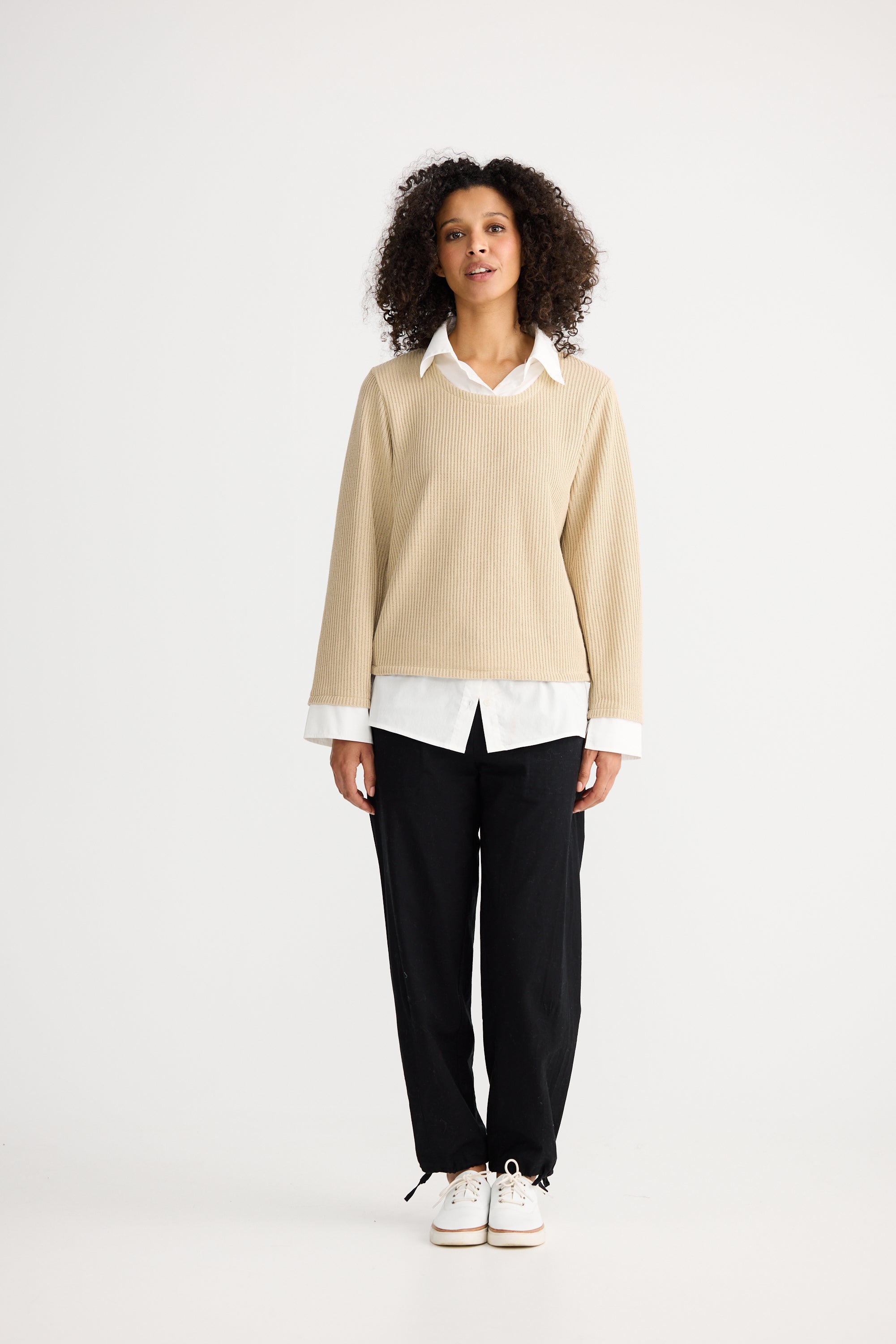 Image of Woman wearing a Shanty Corporation beige sweater over a white shirt with black pants on a white background