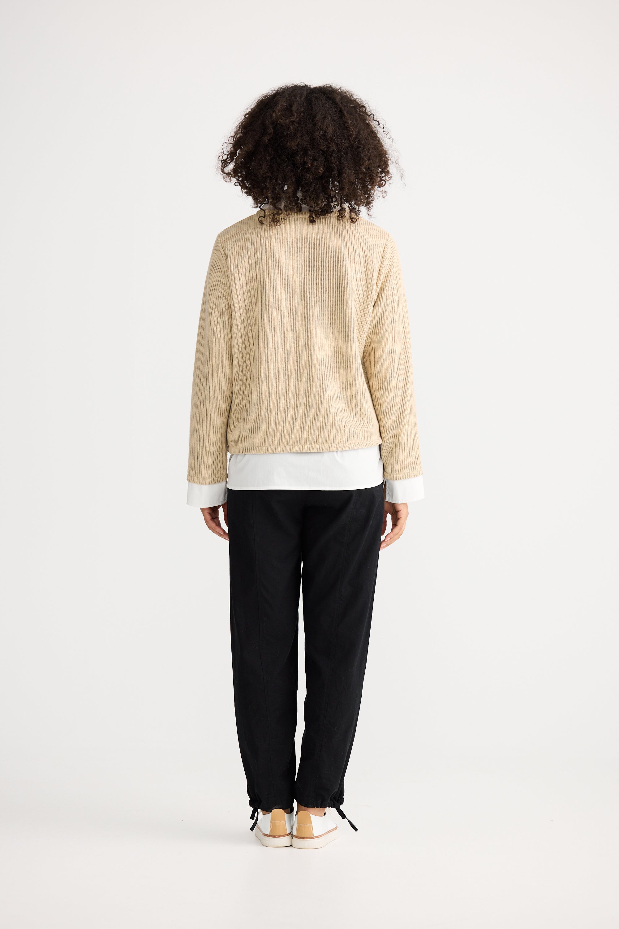 Image of Woman wearing a Shanty Corporation beige sweater over a white shirt with black pants on a white background