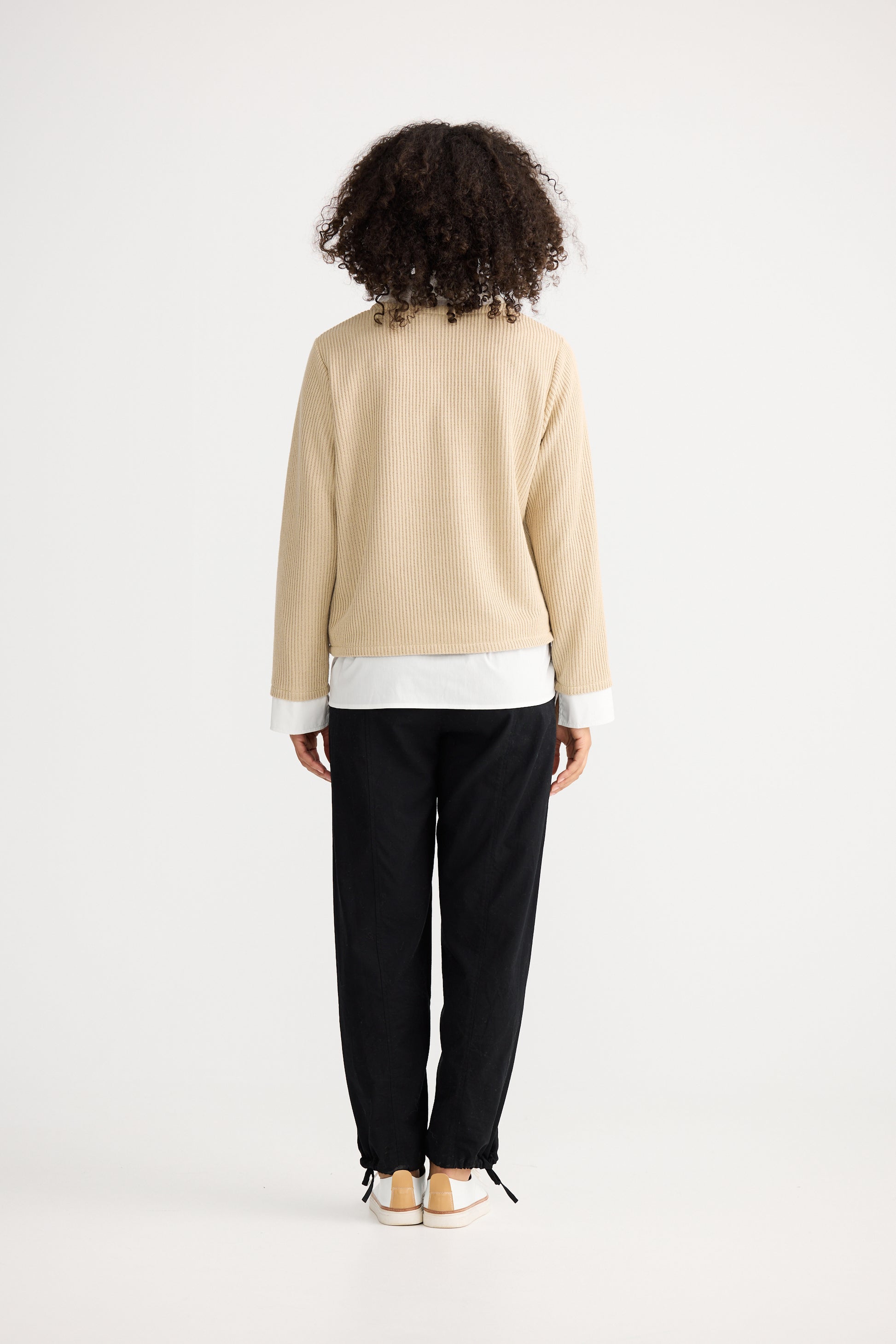 Woman wearing a Shanty Corporation beige sweater over a white shirt with black pants on a white background