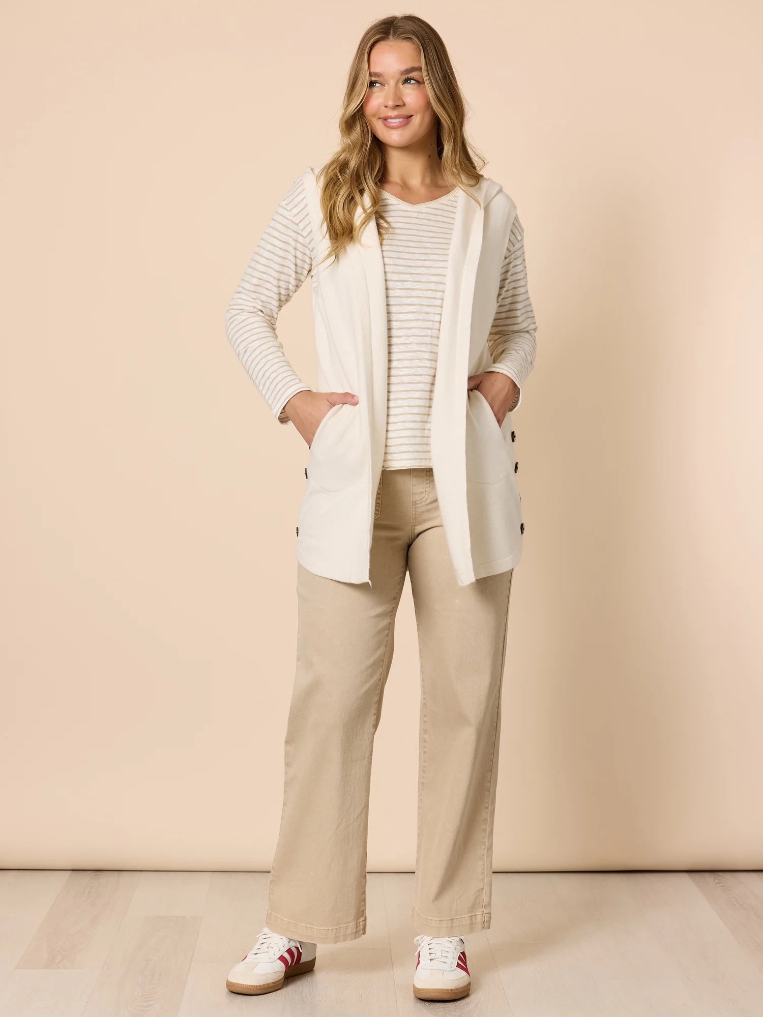 Woman wearing a light gray cardigan, Threadz beige shirt, beige pants, and white sneakers against a beige background