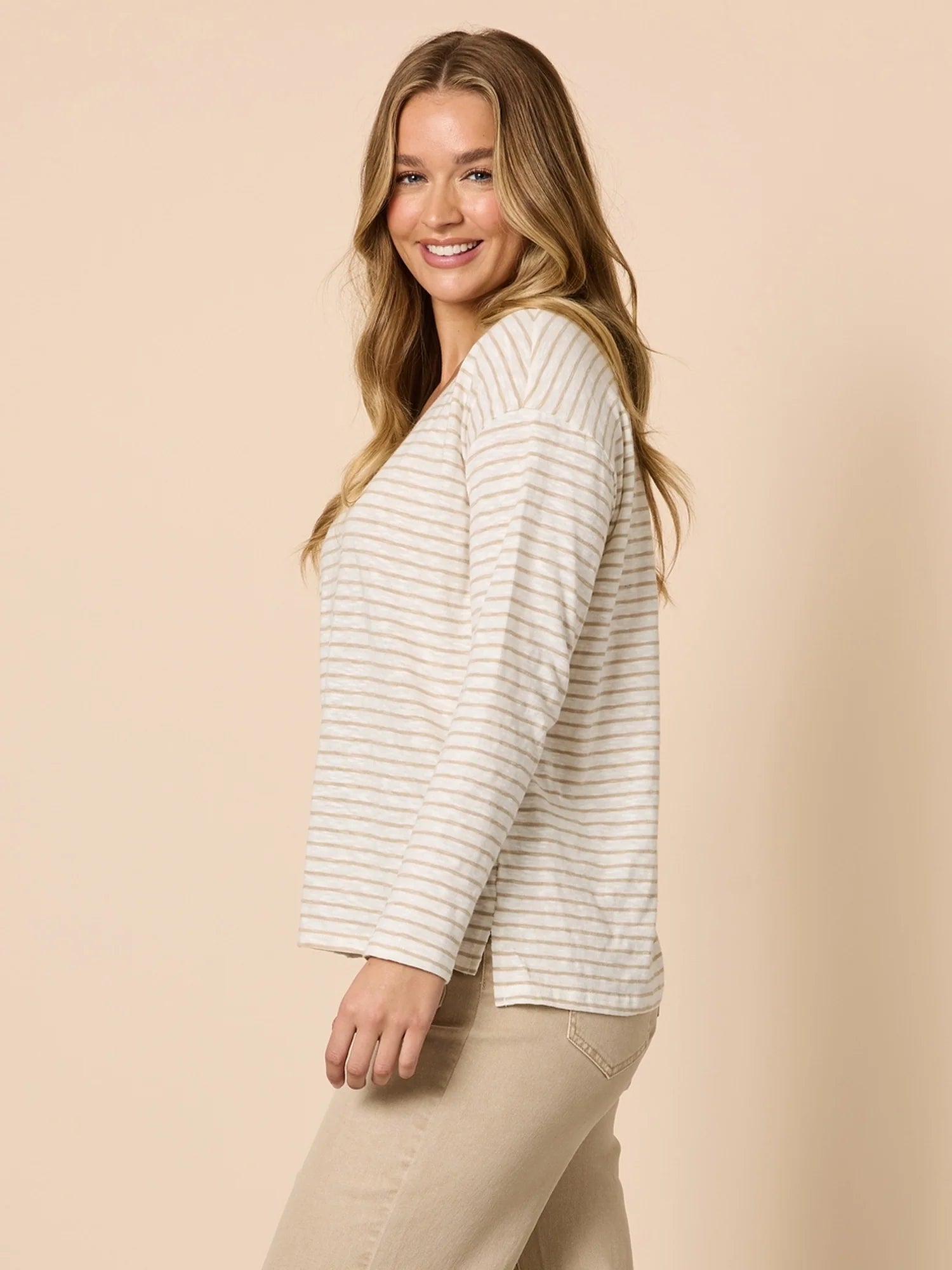Woman wearing a Threadz striped sweater and beige pants against a beige background