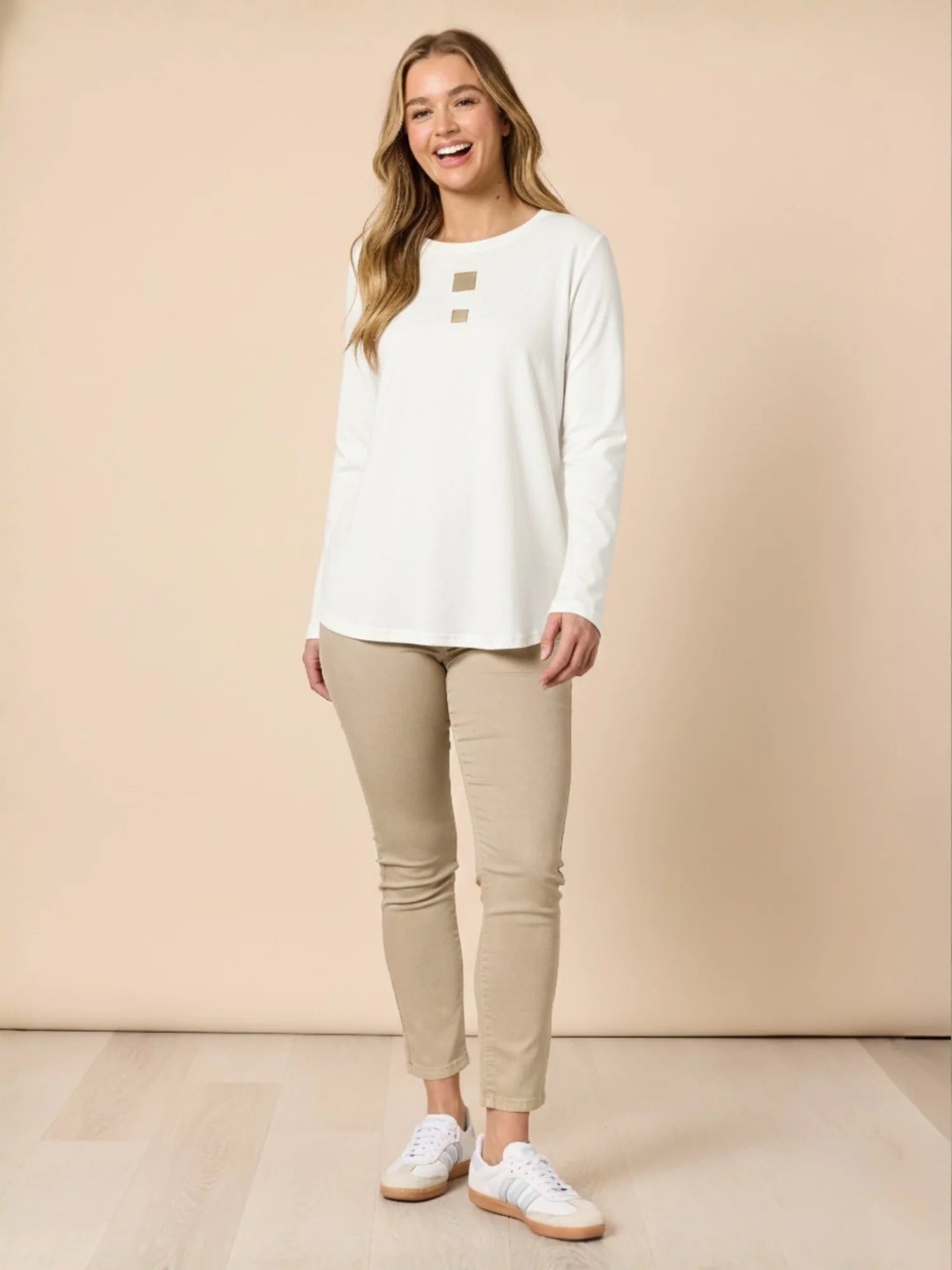 Woman wearing a Threadz white long-sleeve shirt and beige pants on a beige background