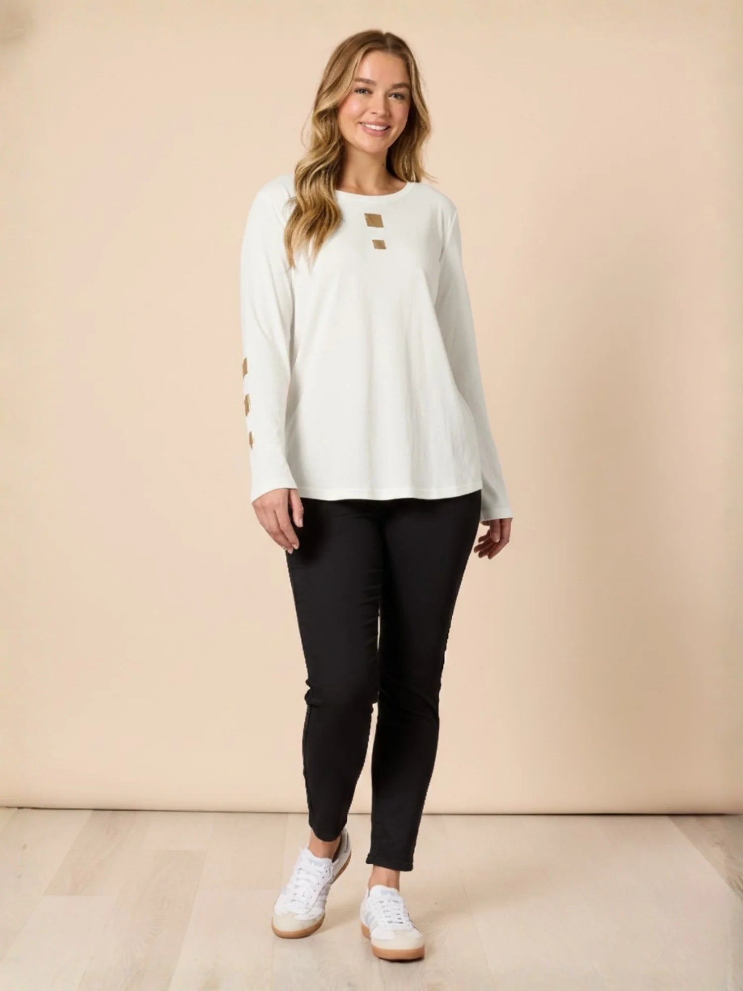 Woman wearing a Threadz white long-sleeve top and black pants against a beige background