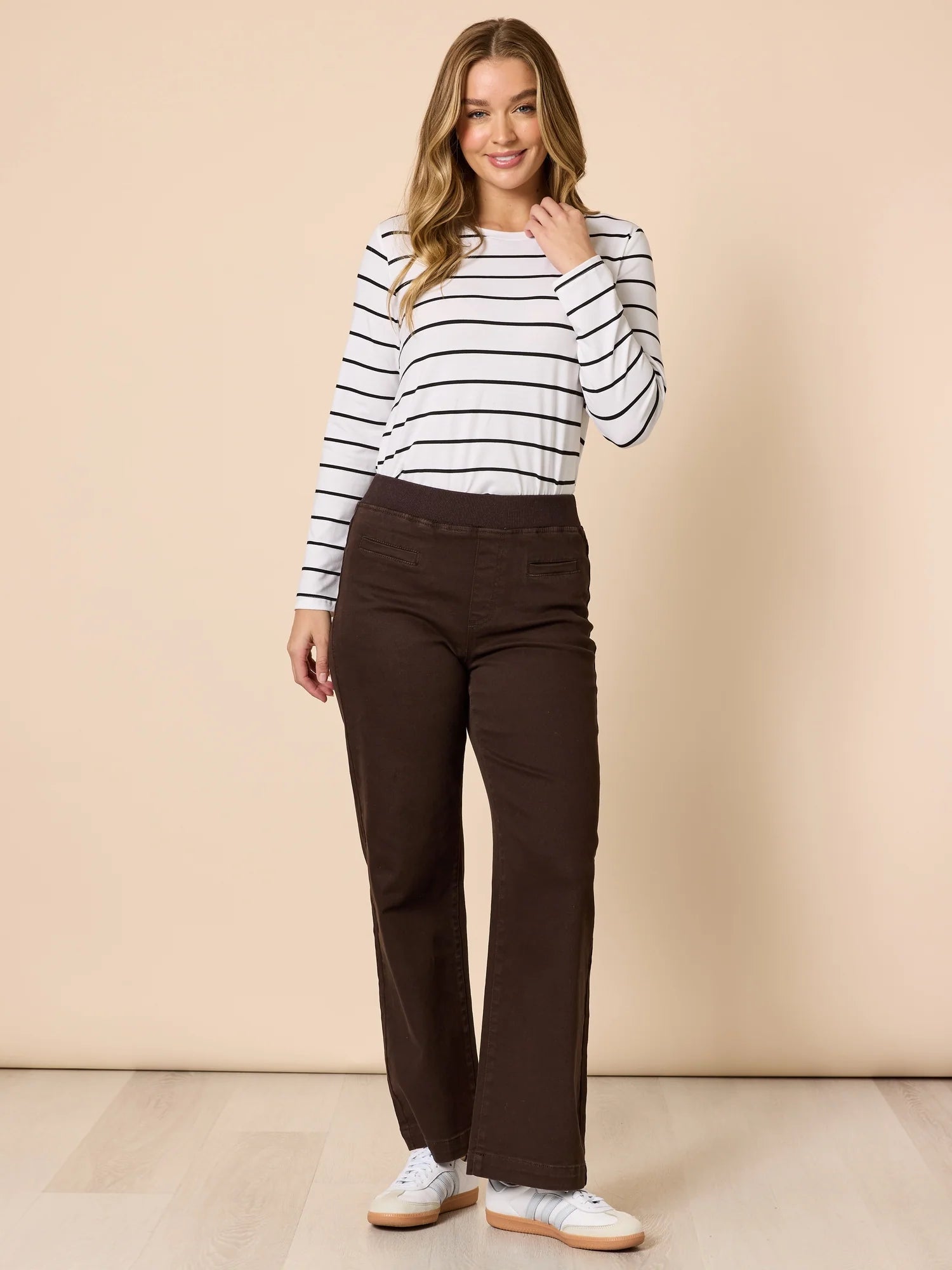 Woman wearing a striped shirt and Threadz brown pants against a beige background