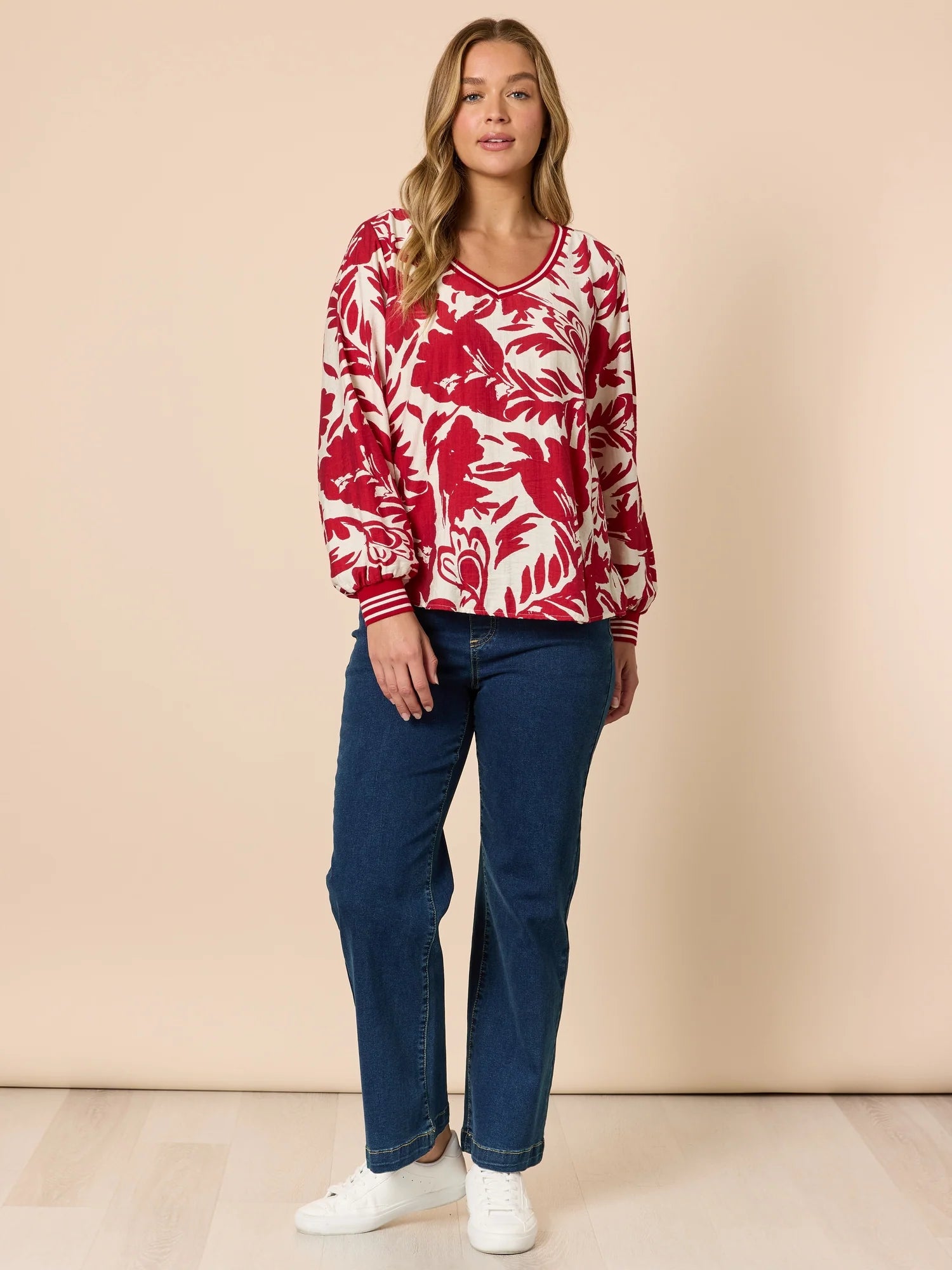 Woman wearing a red and white patterned top with Threadz blue jeans on a beige background