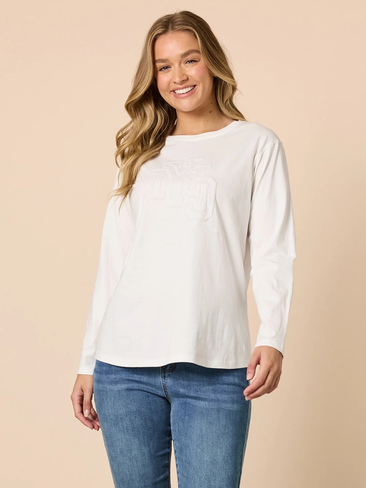Woman wearing Threadz white long-sleeve top and blue jeans on a beige background
