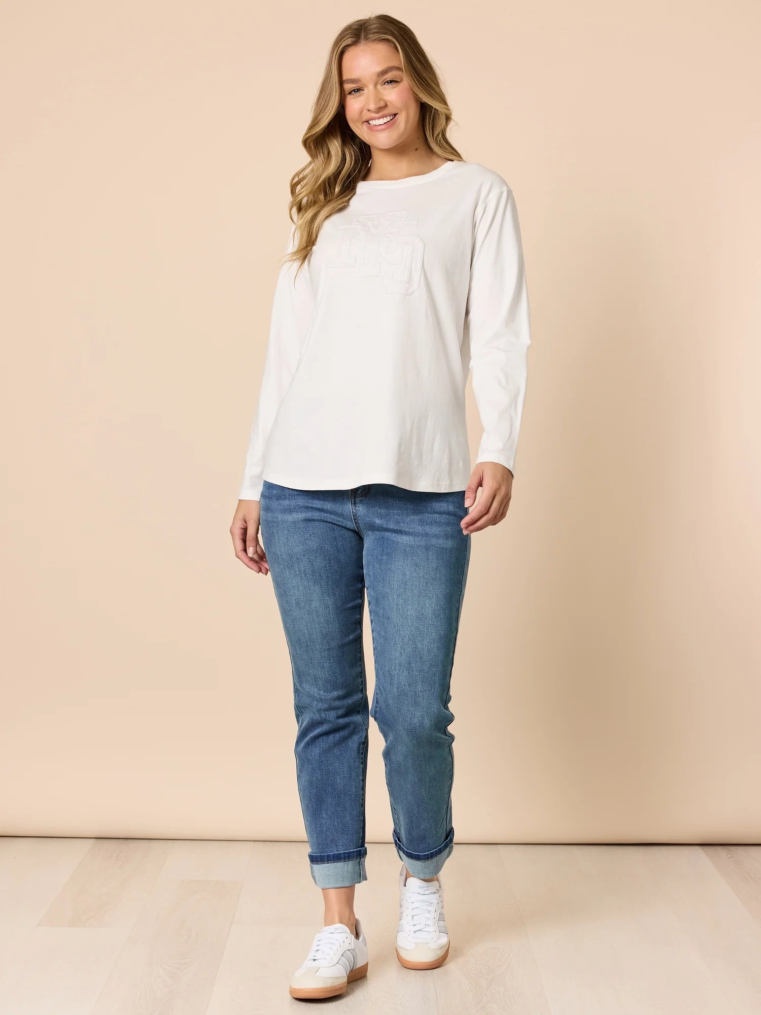 Woman wearing Threadz white long-sleeve top and blue jeans on a beige background