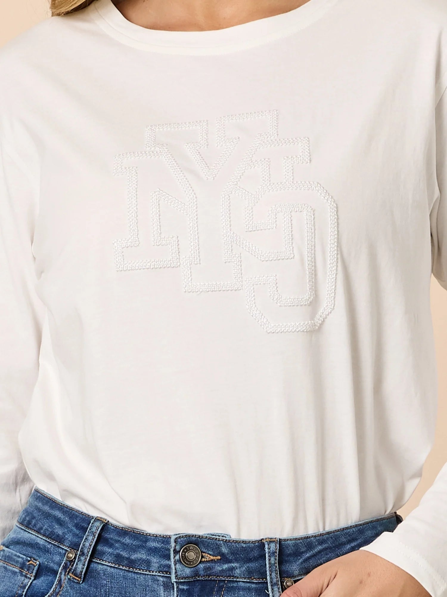 Close-up of a person wearing Threadz white long-sleeve shirt and blue jeans.