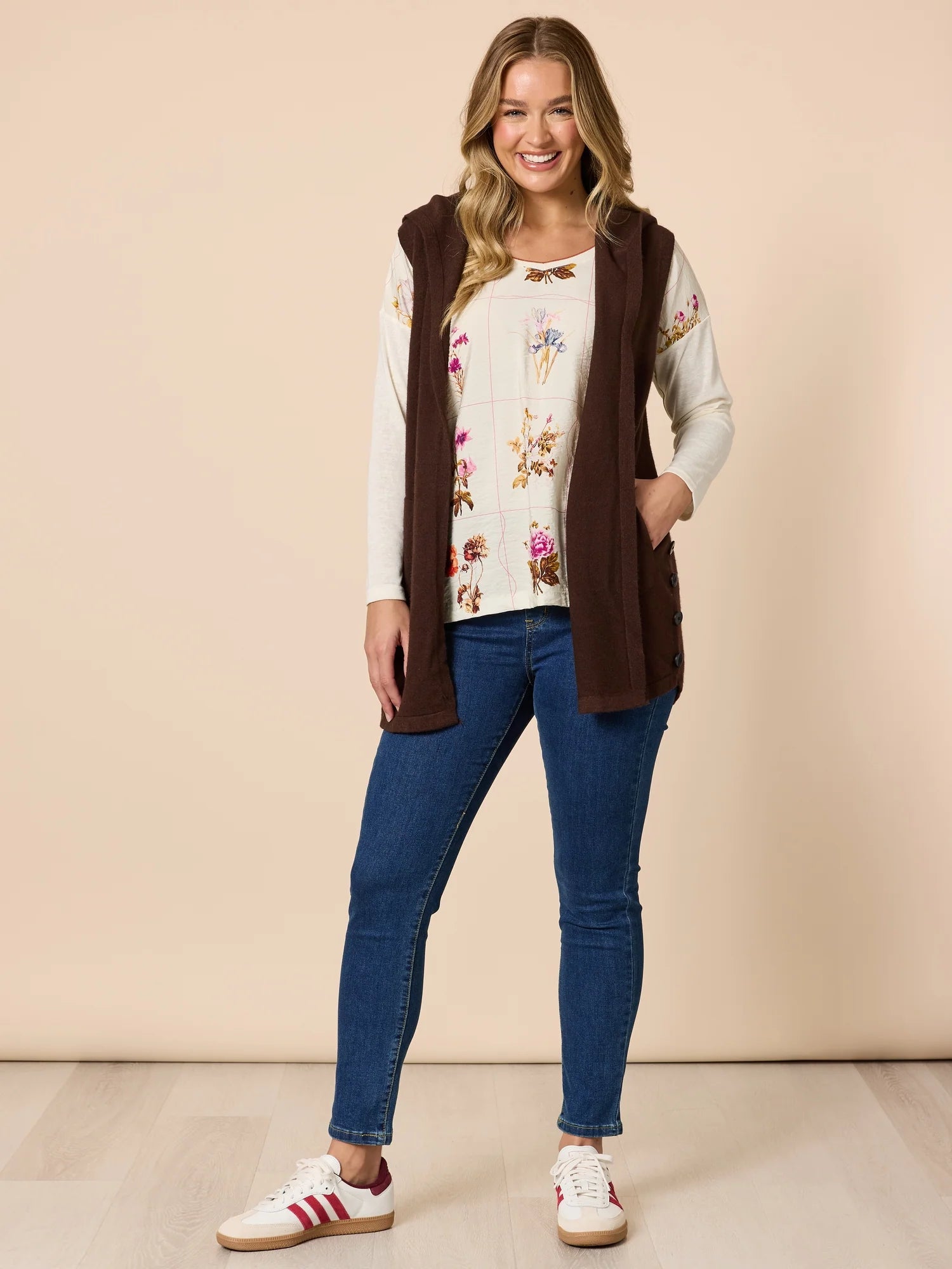 Woman wearing a Threadz brown vest, floral top, and blue jeans against a beige background