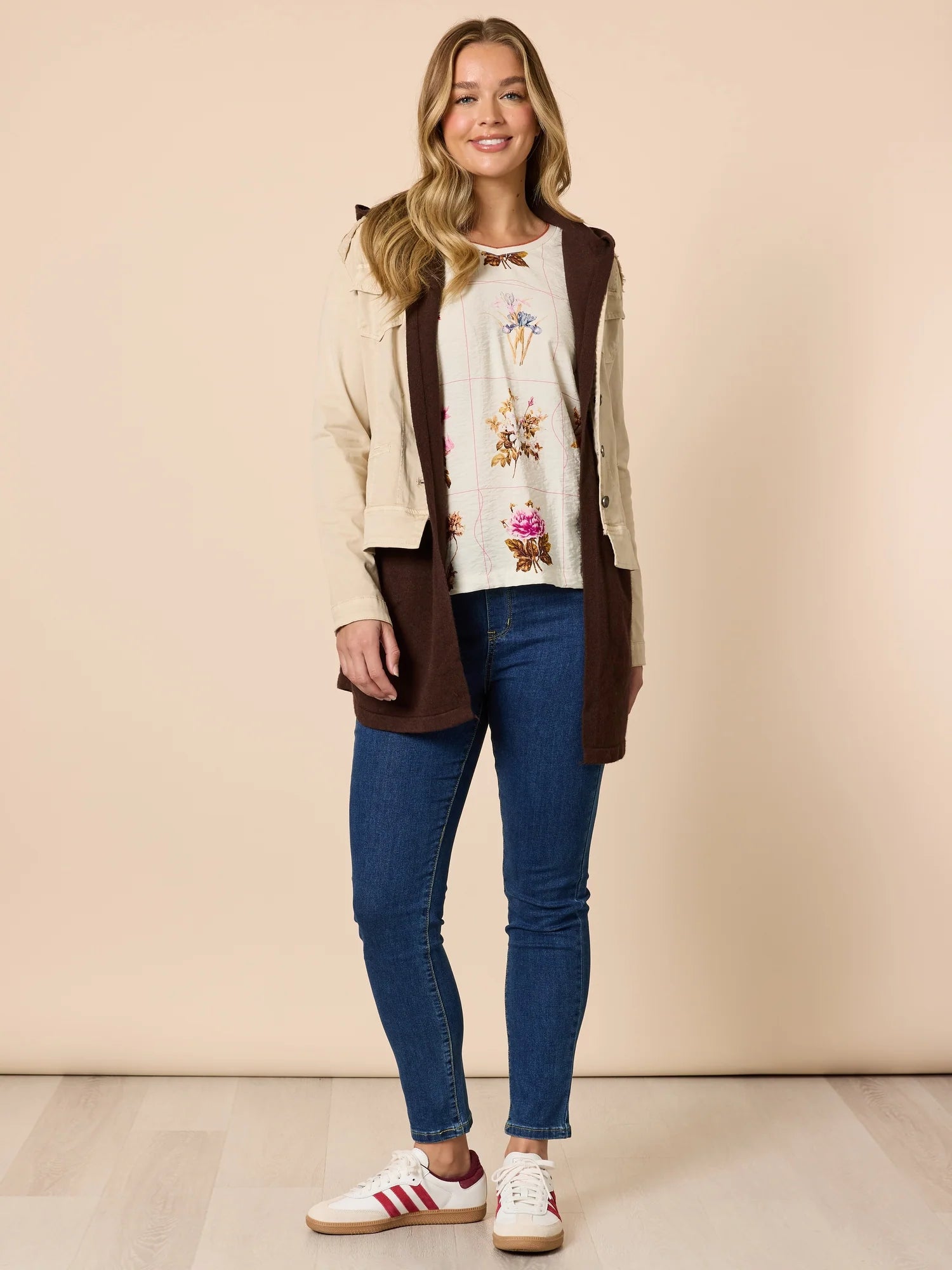 Woman wearing a Threadz brown vest, floral top, and blue jeans against a beige background