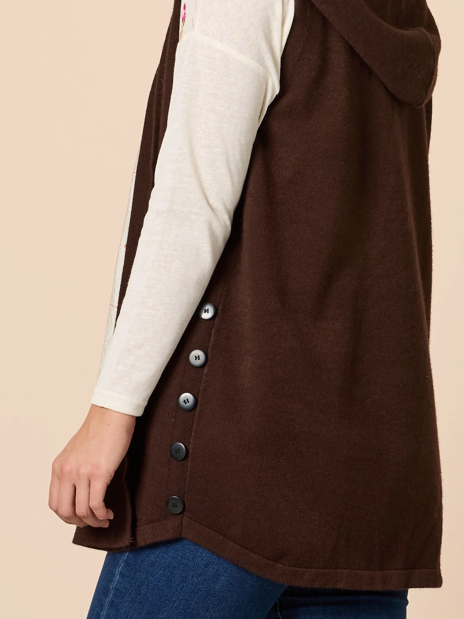 Threadz Brown vest with buttons worn over a white long-sleeve shirt and blue jeans on a beige background