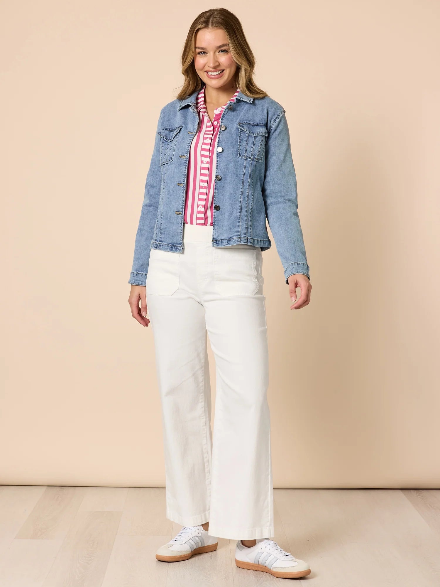Woman wearing a Threadz denim jacket, striped shirt, and white pants on a beige background