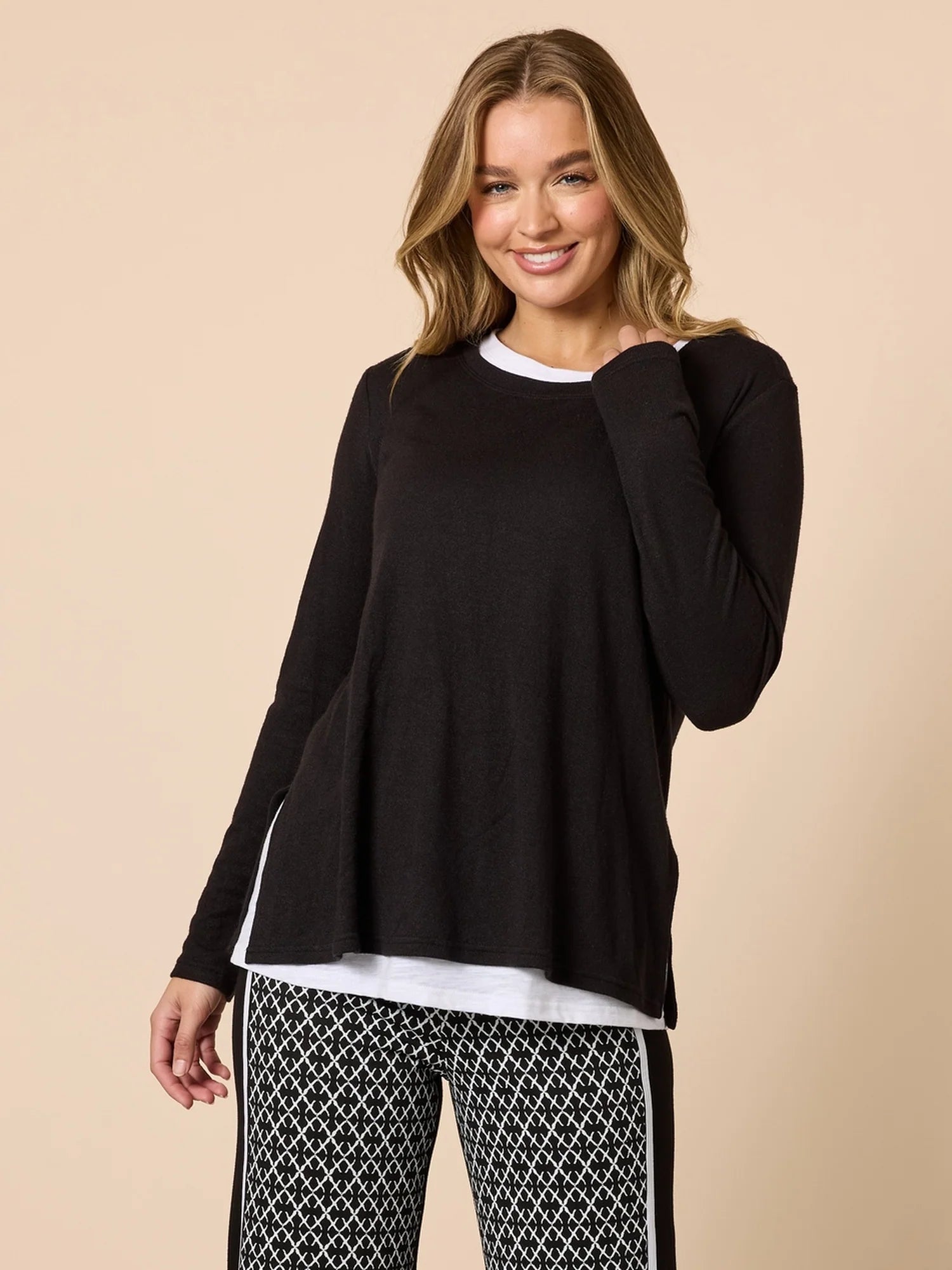 Image of Woman wearing a Threadz black long-sleeve top over a white shirt with patterned pants on a beige background