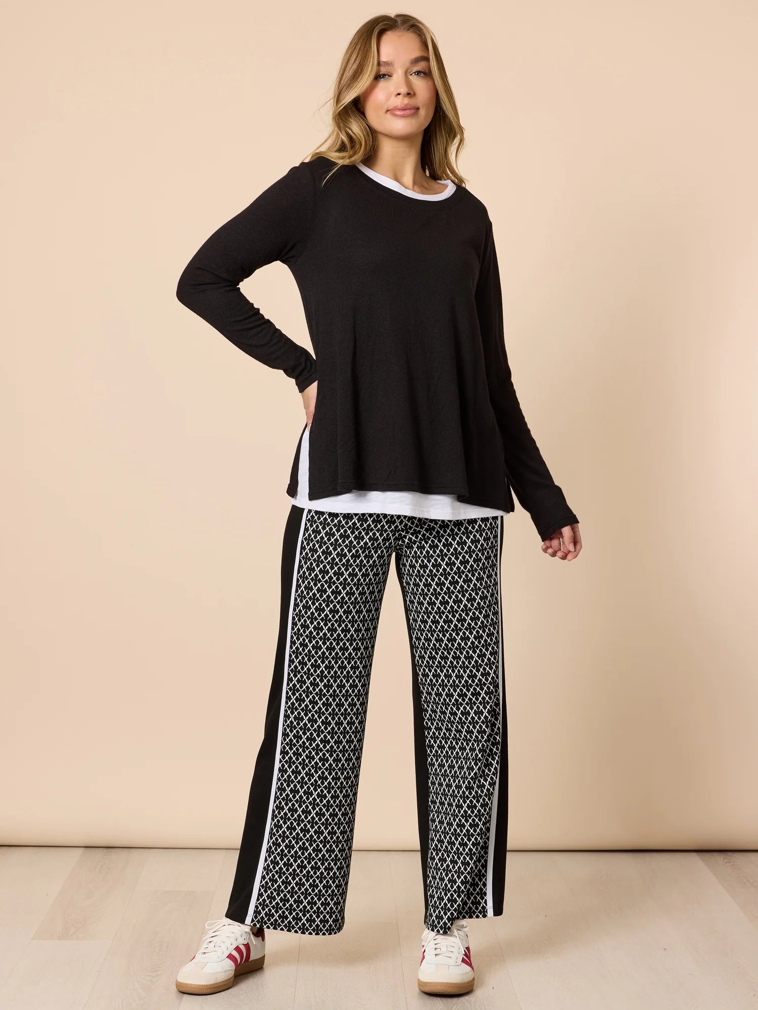 Woman wearing a Threadz black long-sleeve top and patterned pants on a beige background