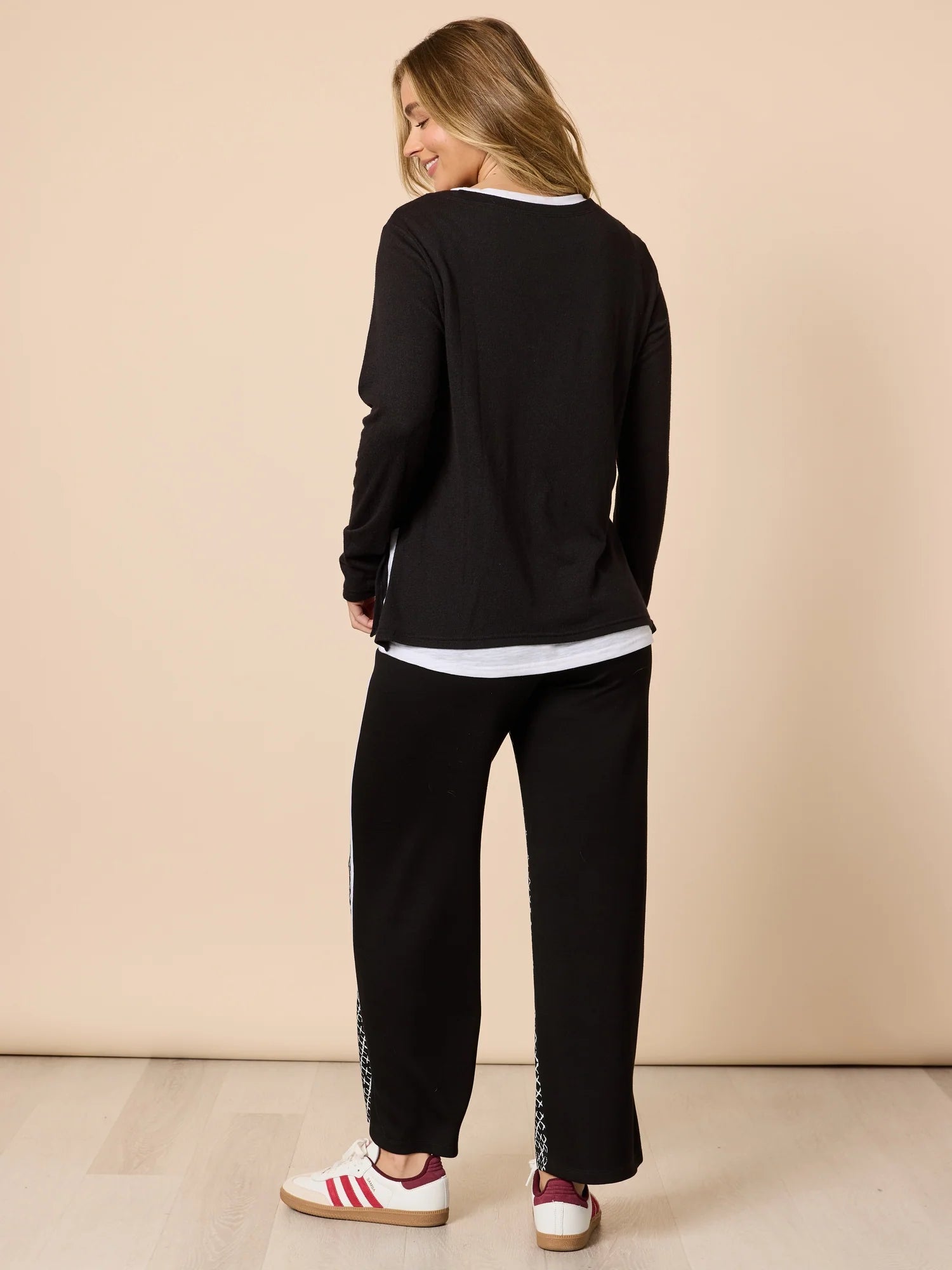 Image of Woman wearing a Threadz black tracksuit with white stripes on a beige background