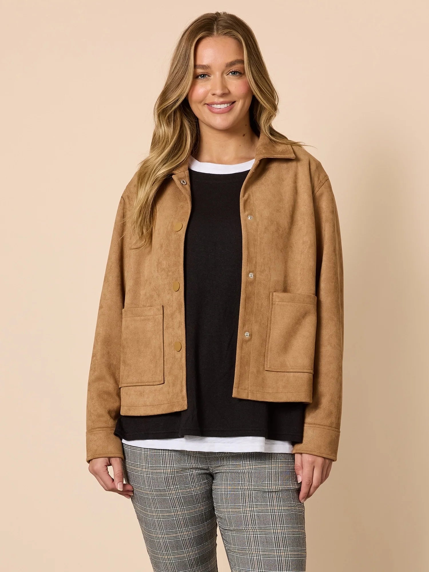 Image of Woman wearing a brown jacket over a Threadz black top and plaid pants on a beige background