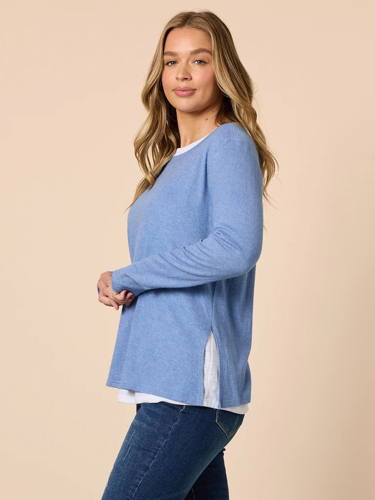 Woman wearing a Threadz blue sweater over a white shirt with jeans on a beige background