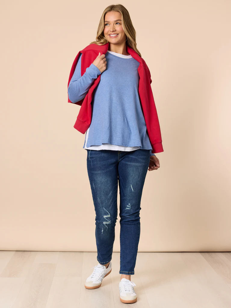 Woman wearing a Threadz blue sweater, red jacket, and jeans on a beige background