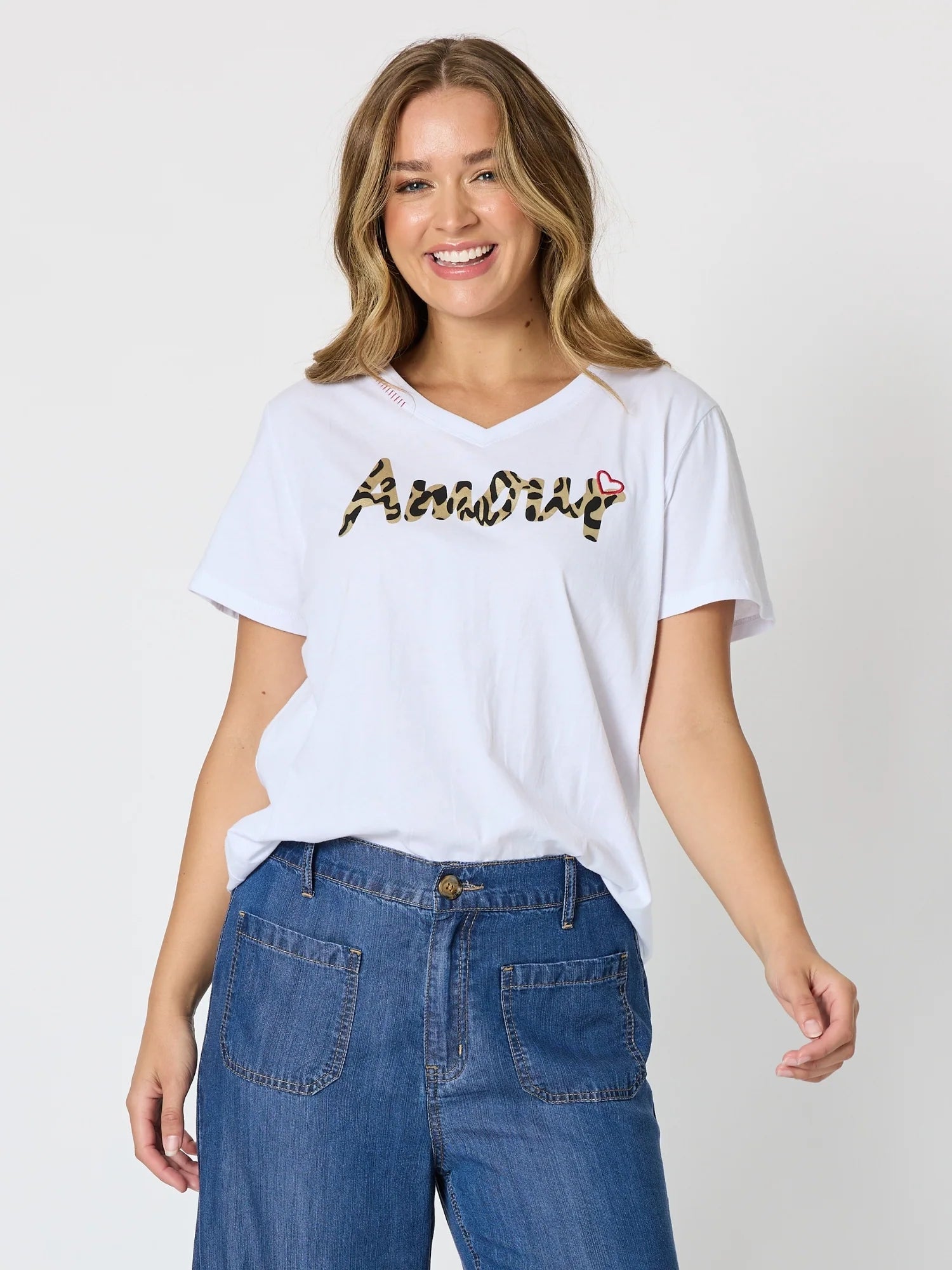 Image of A woman wearing a Threadz white v-neck t-shirt with a stylized 'AmoDip' logo across the chest in a camouflage pattern with a small red rose accent, paired with blue jeans, against a light gray studio background.