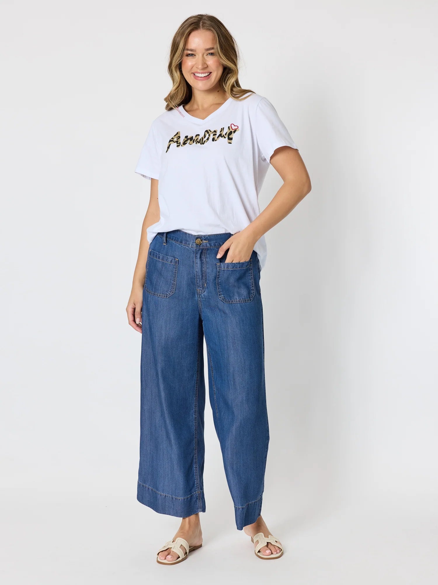 Image of A woman modeling a Threadz white short-sleeve t-shirt with a black script graphic on the chest, paired with wide-leg blue denim jeans and beige flat sandals, against a plain light gray studio background.
