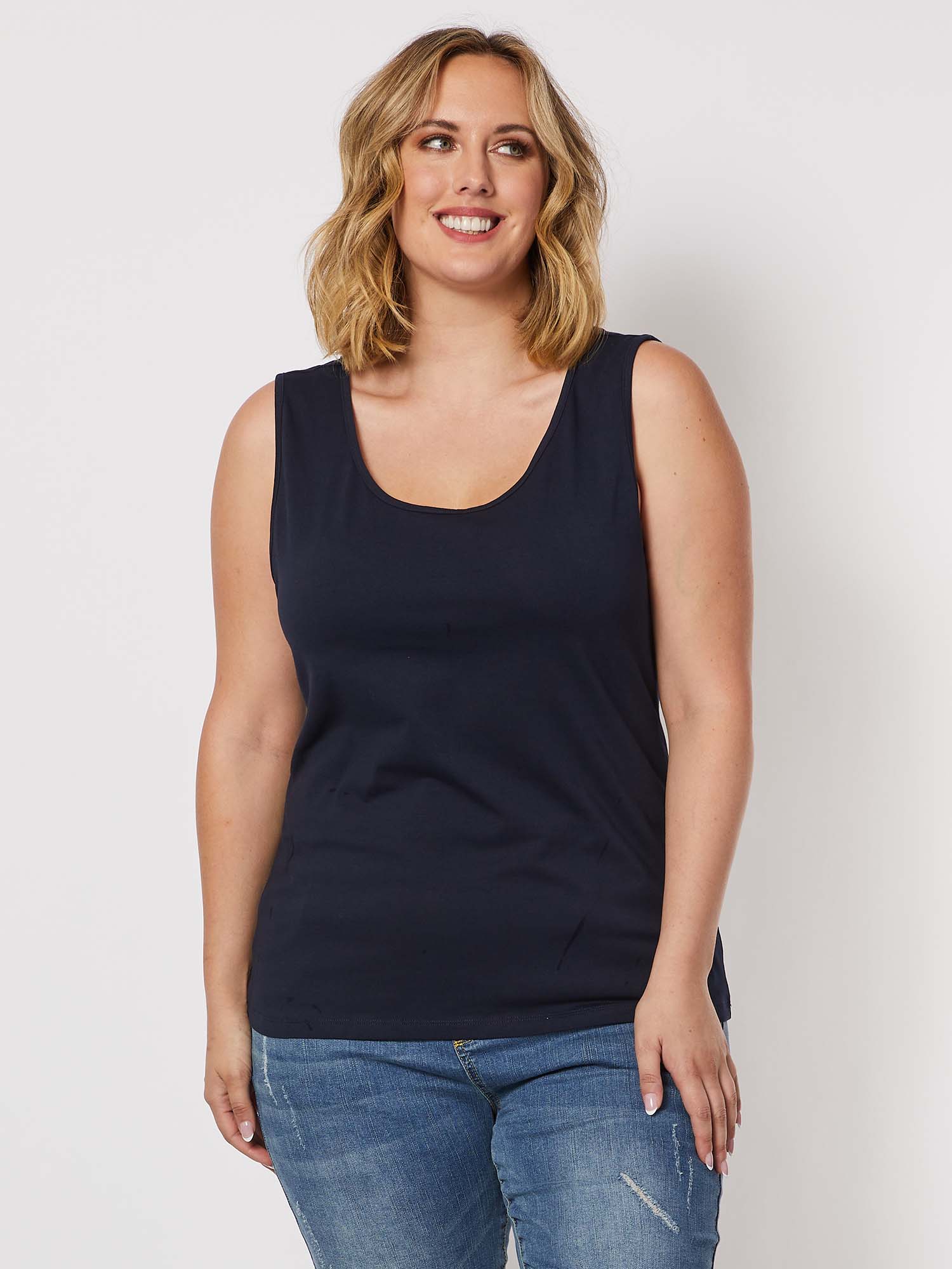 Image of A woman modeling a Threadz sleeveless scoop-neck tank top in dark navy blue, paired with blue jeans, against a plain light gray studio background.