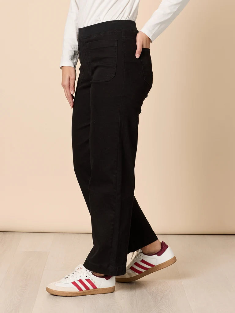 Woman wearing Threadz black pants and white sneakers with red stripes on a beige background