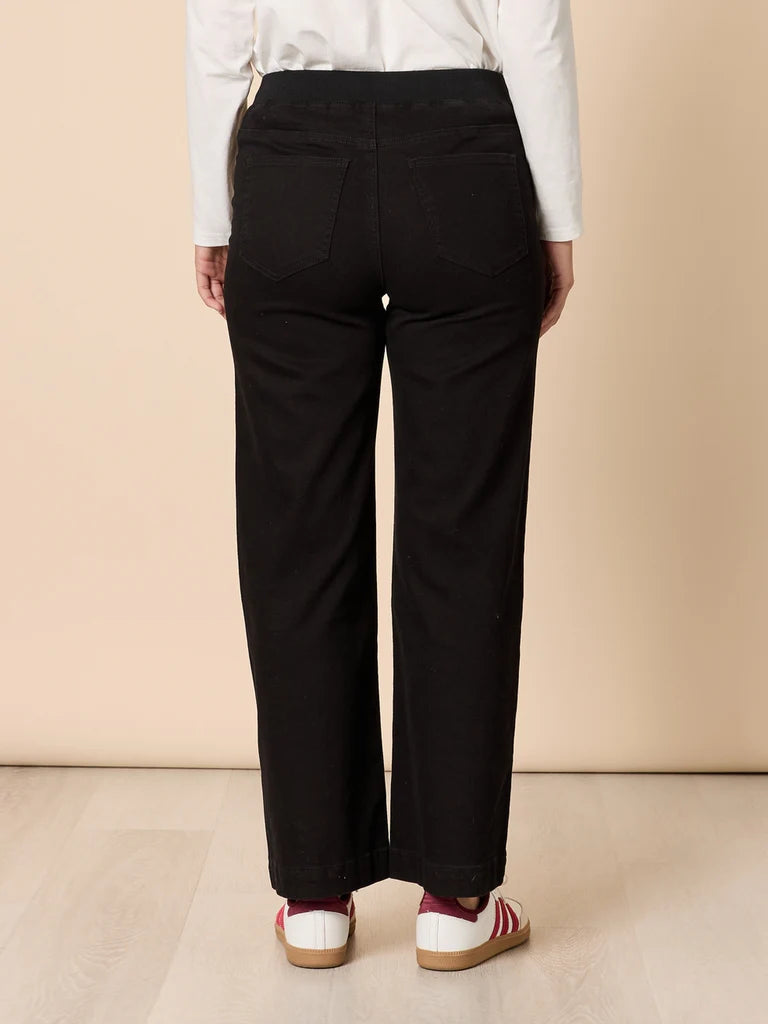 Woman wearing Threadz black pants and a white shirt on a beige background