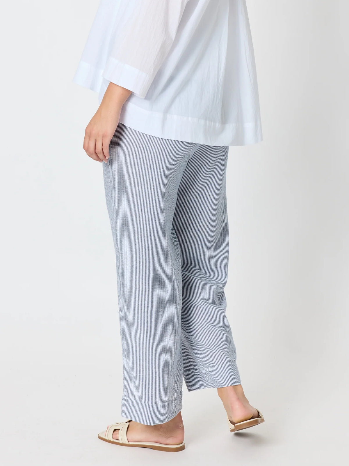 A woman shown from the back wearing Threadz light blue and white vertically striped wide-leg cropped pants, a white blouse, and beige slide sandals against a plain light gray studio background.