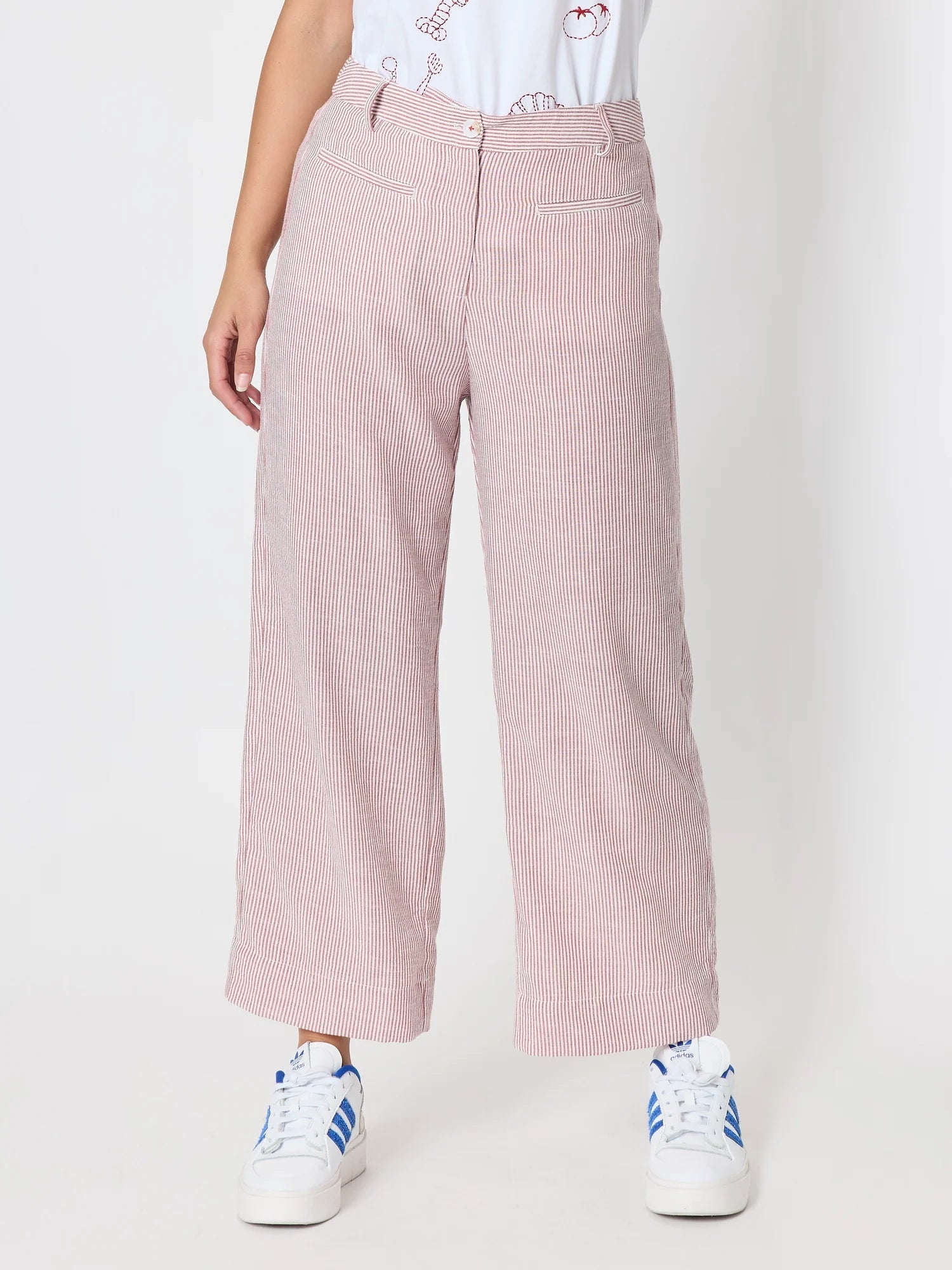 Image of A woman wearing Threadz light pink wide-leg cropped pants with a subtle vertical stripe texture, styled with a white graphic t-shirt and white sneakers with blue stripes, against a plain white studio background.